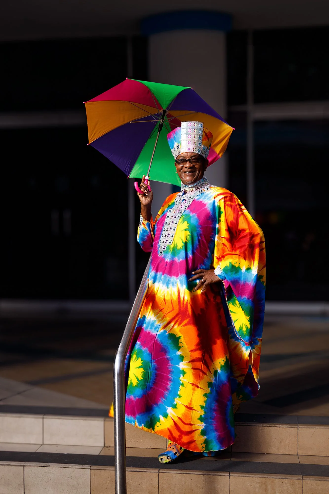 Portrait of a Barbados Pride attendee wearing vibrant rainbow clothing and holding a colorful umbrella during the celebration in Bridgetown.
