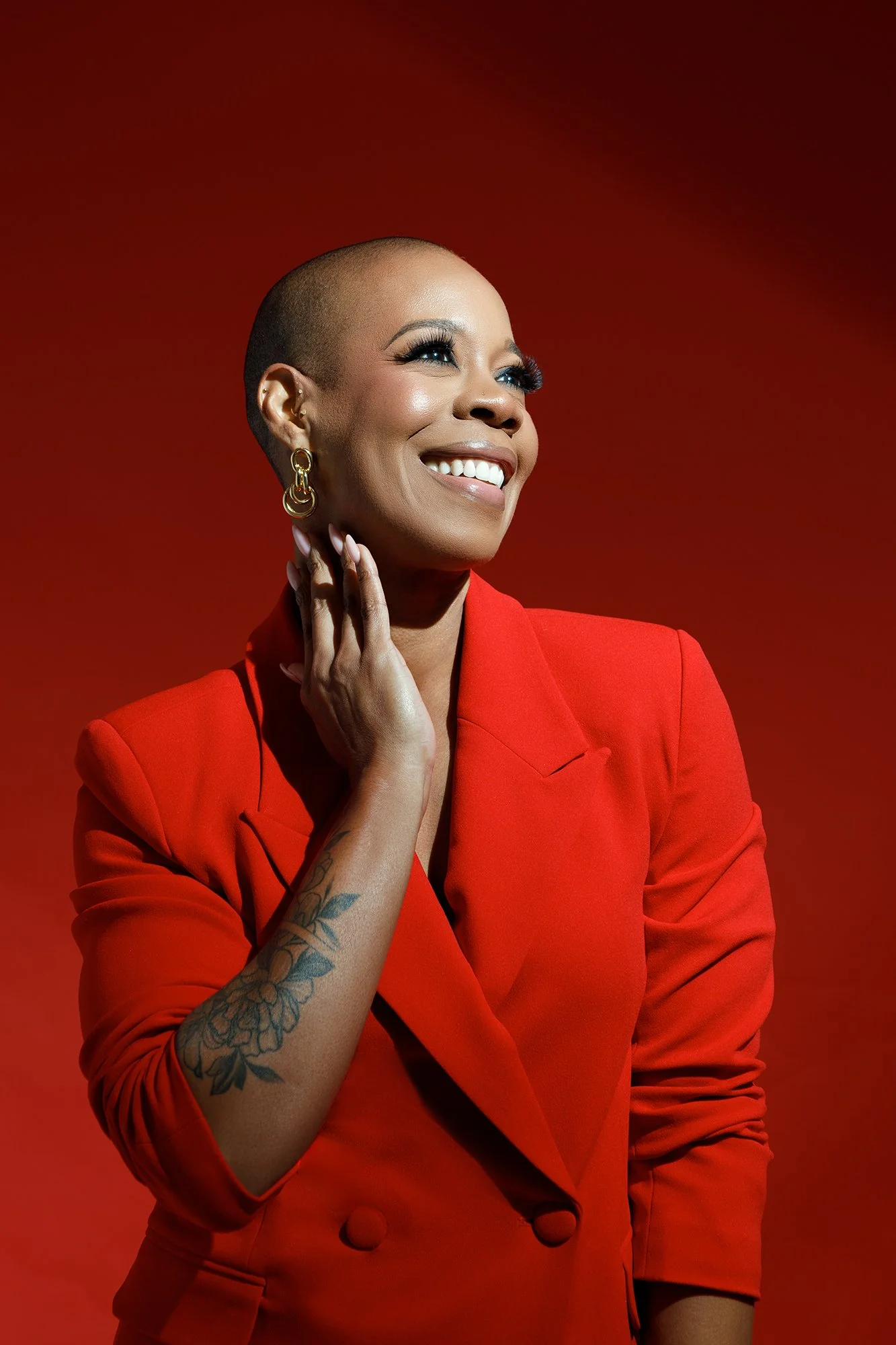 Editorial portrait of a smiling woman in a tailored red blazer with warm studio lighting against a vibrant red background, photographed by Alyson Holder.