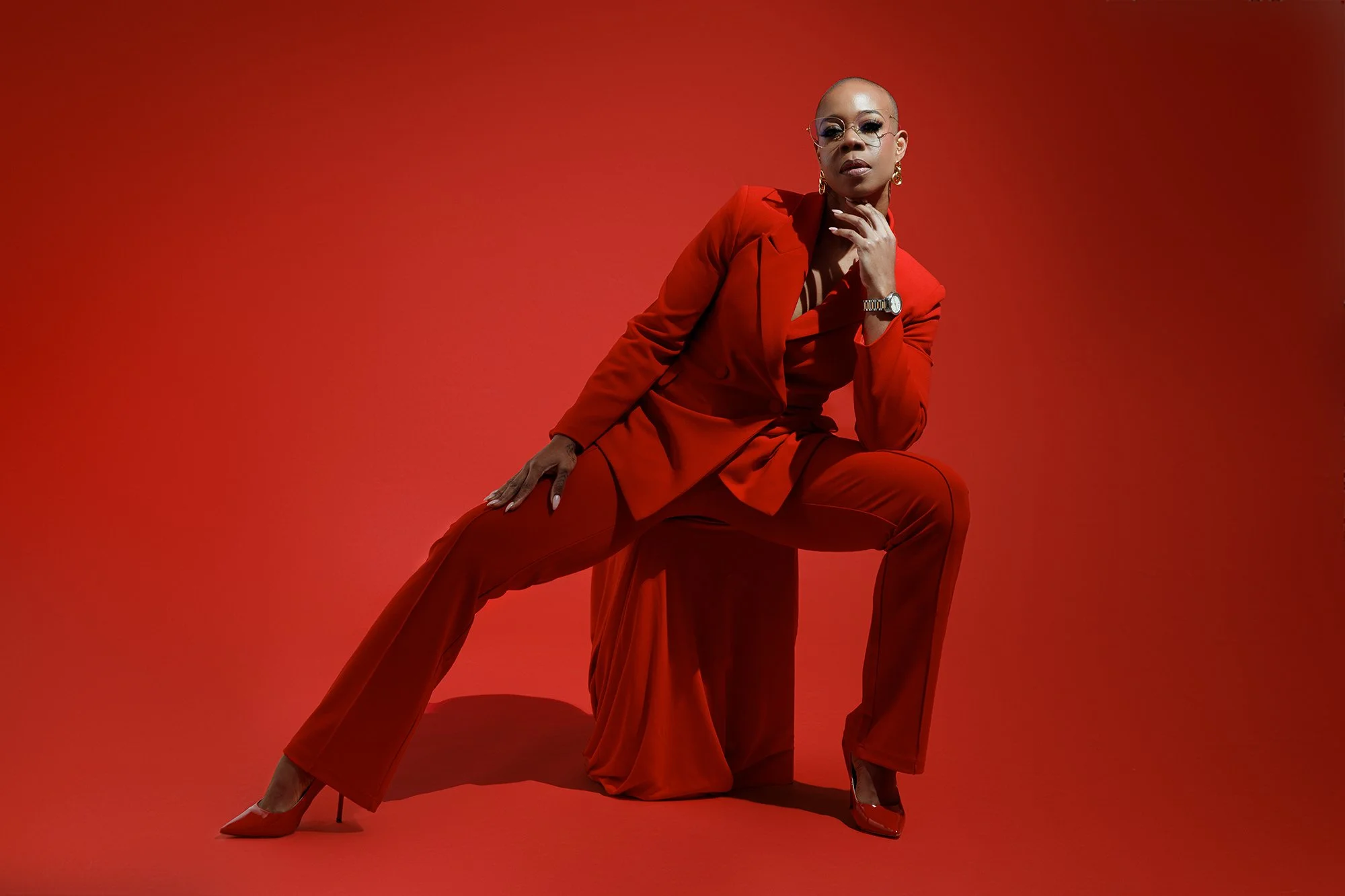 Fashion-inspired portrait of a woman in a red tailored suit posing in a commercial studio with dramatic directional lighting.
