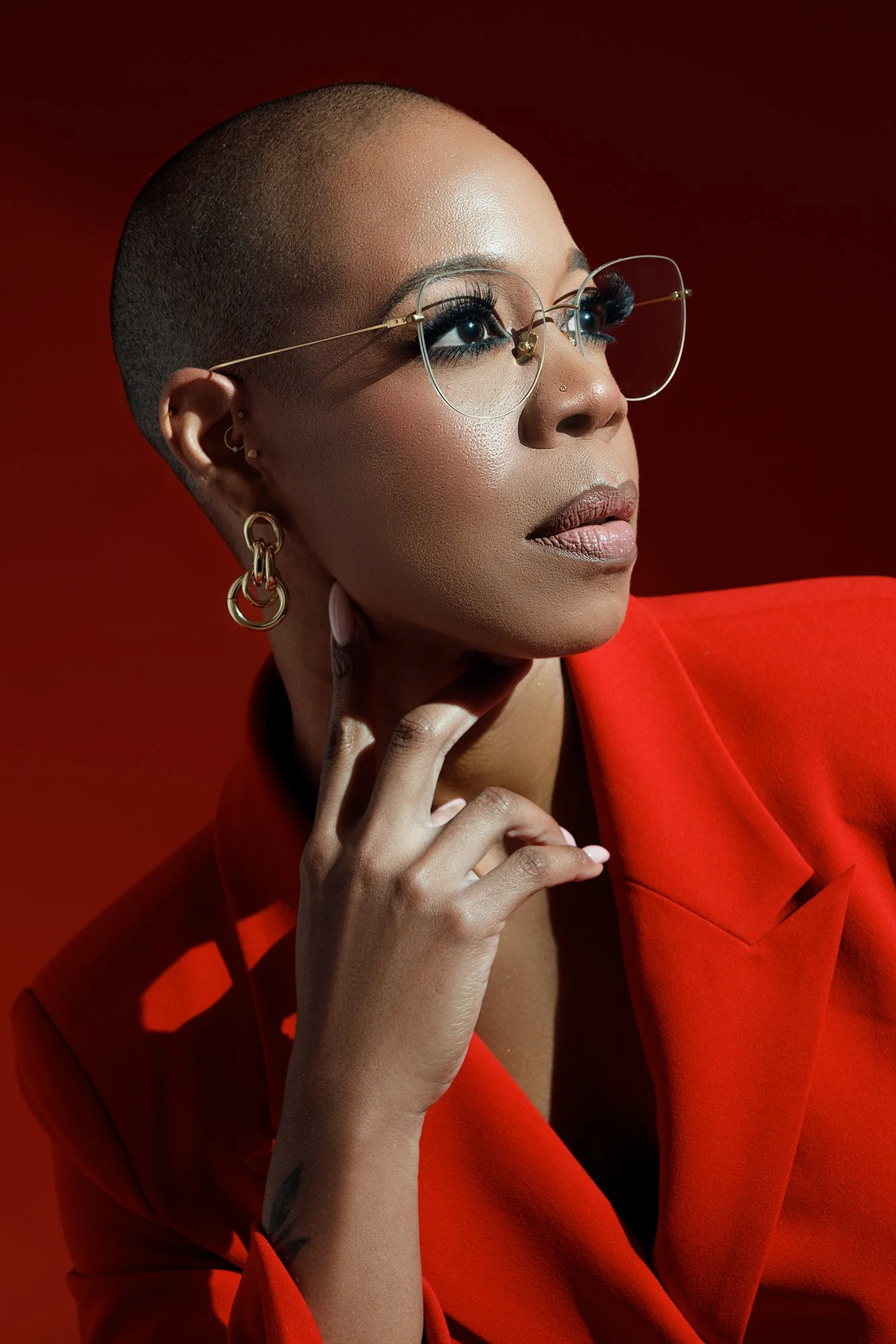Close-up editorial headshot of a woman wearing glasses and a tailored red blazer against a monochromatic red background.