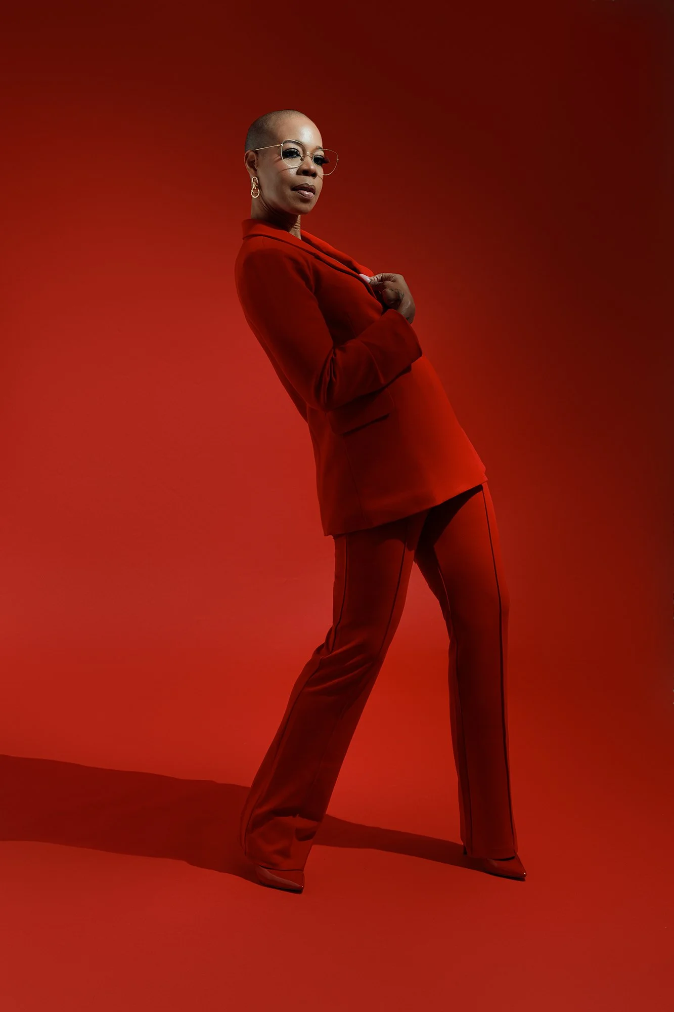 Full-length editorial portrait of a woman wearing a tailored red suit against a monochromatic red studio backdrop, photographed by Alyson Holder.