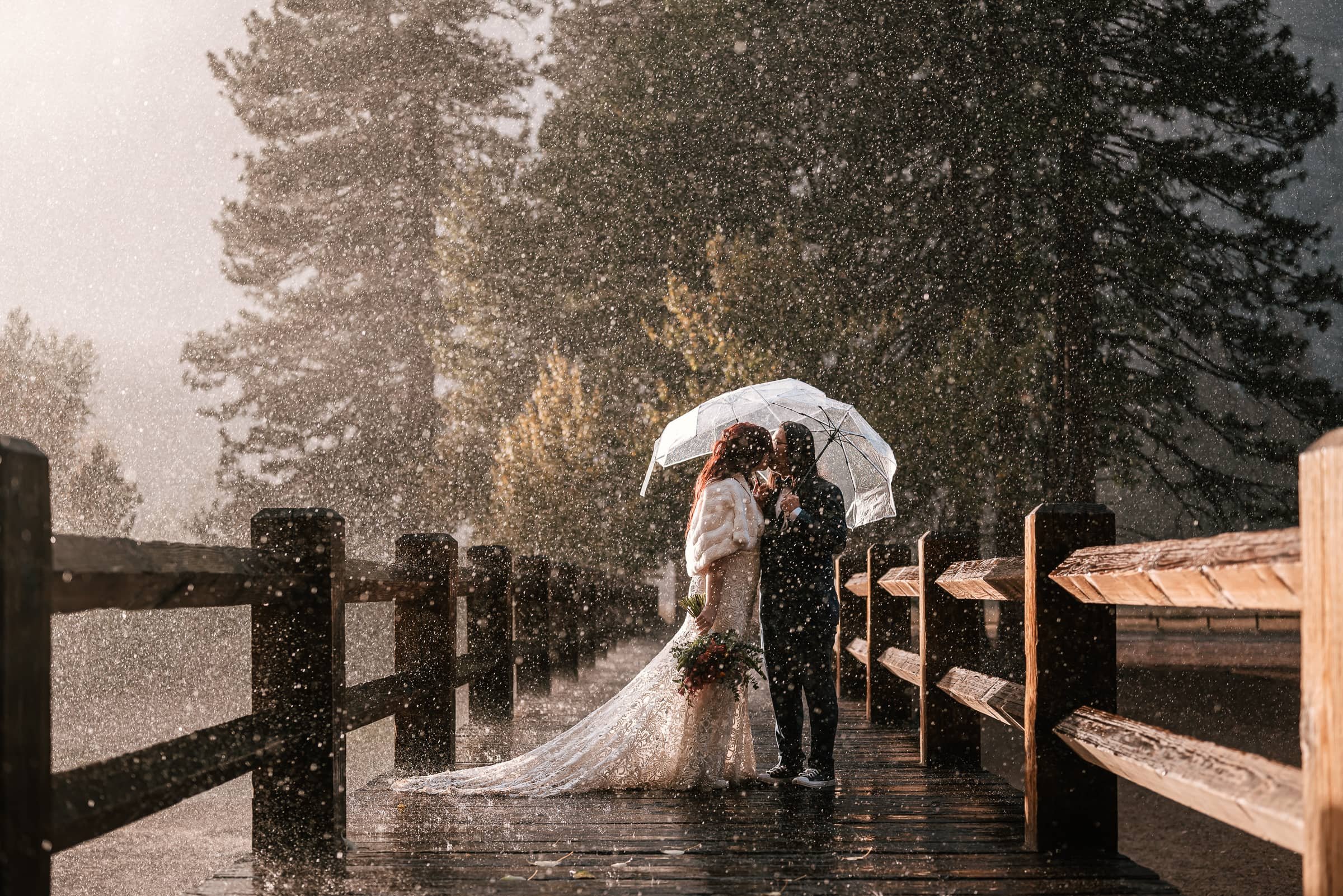 rain falls on married couples clear umbrella while hiking yosemite