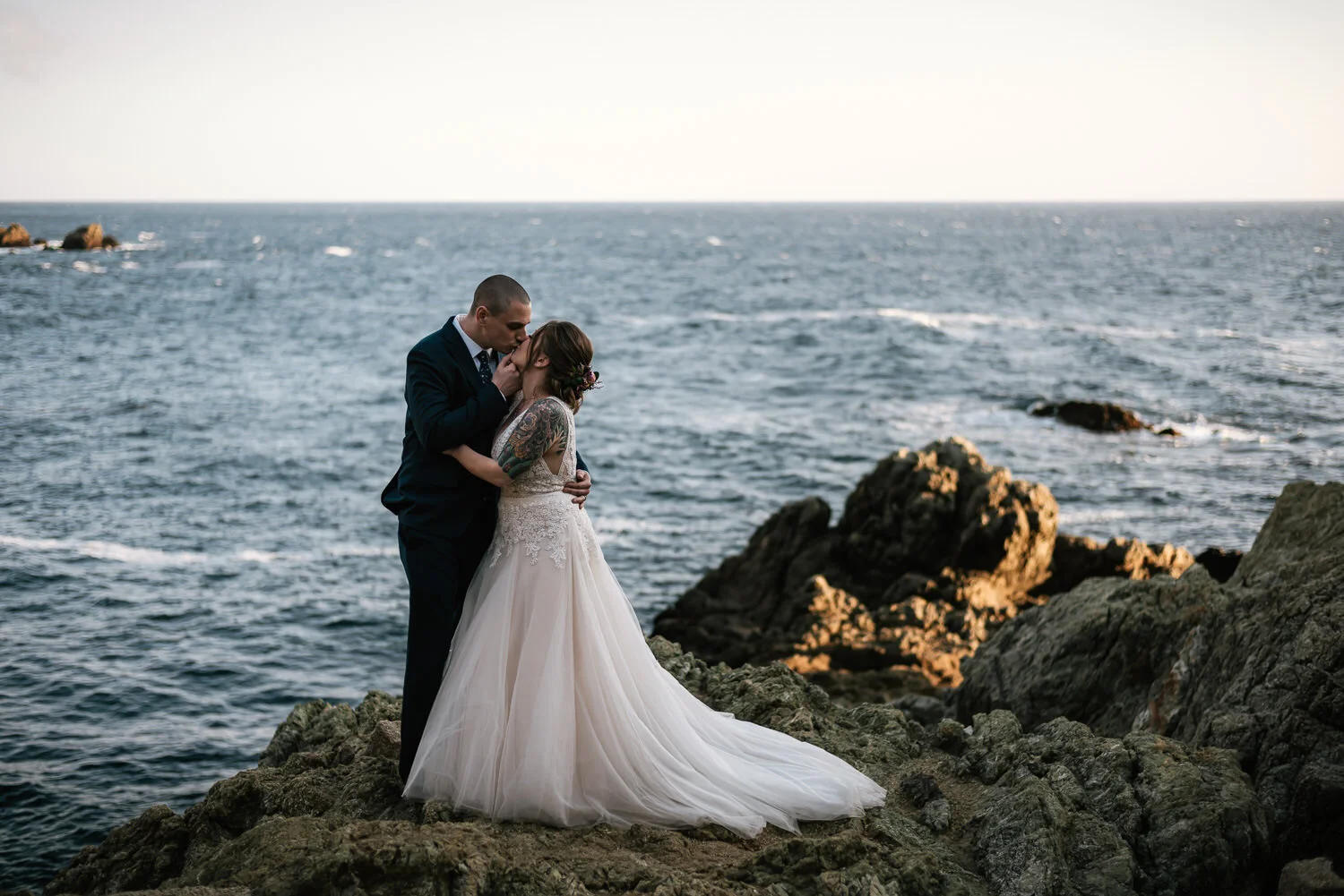 tender kiss between bride and groom on rocks of big sur