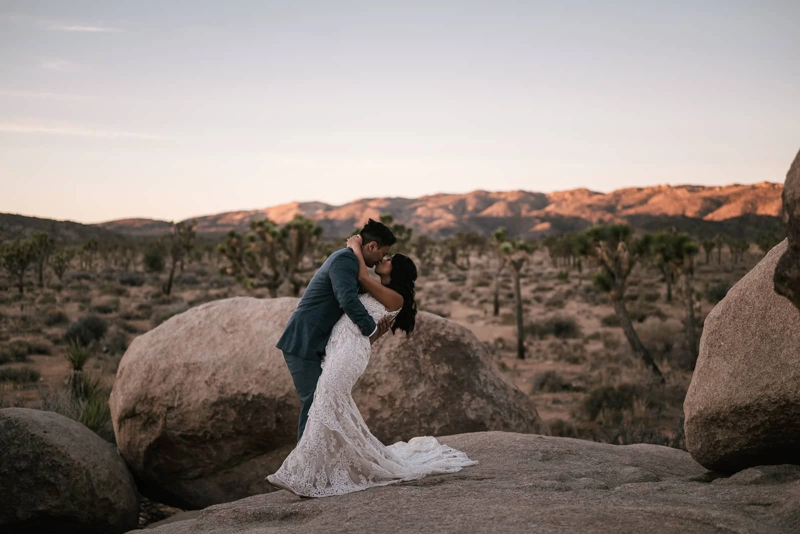 groom kisses bride on desert rocks