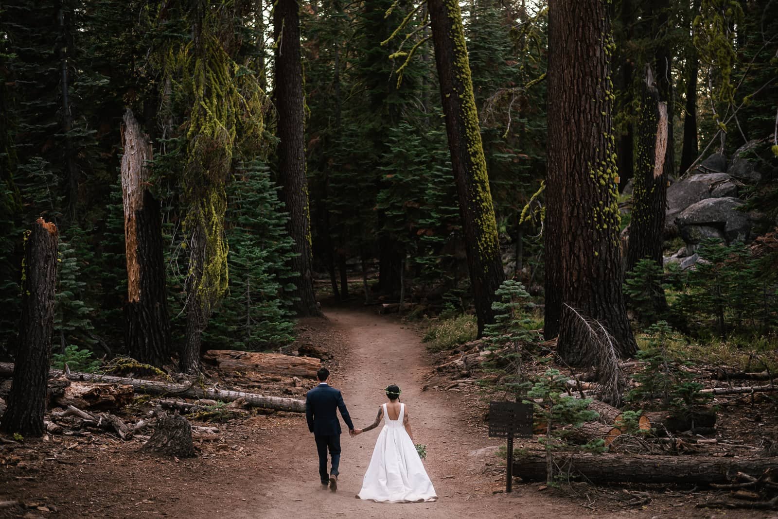 couple walks hand in hand down trail in wedding attire