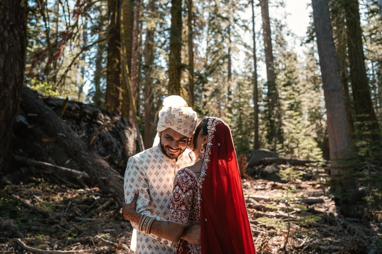 bride in traditional wedding attire whispers in husband's ear in forest