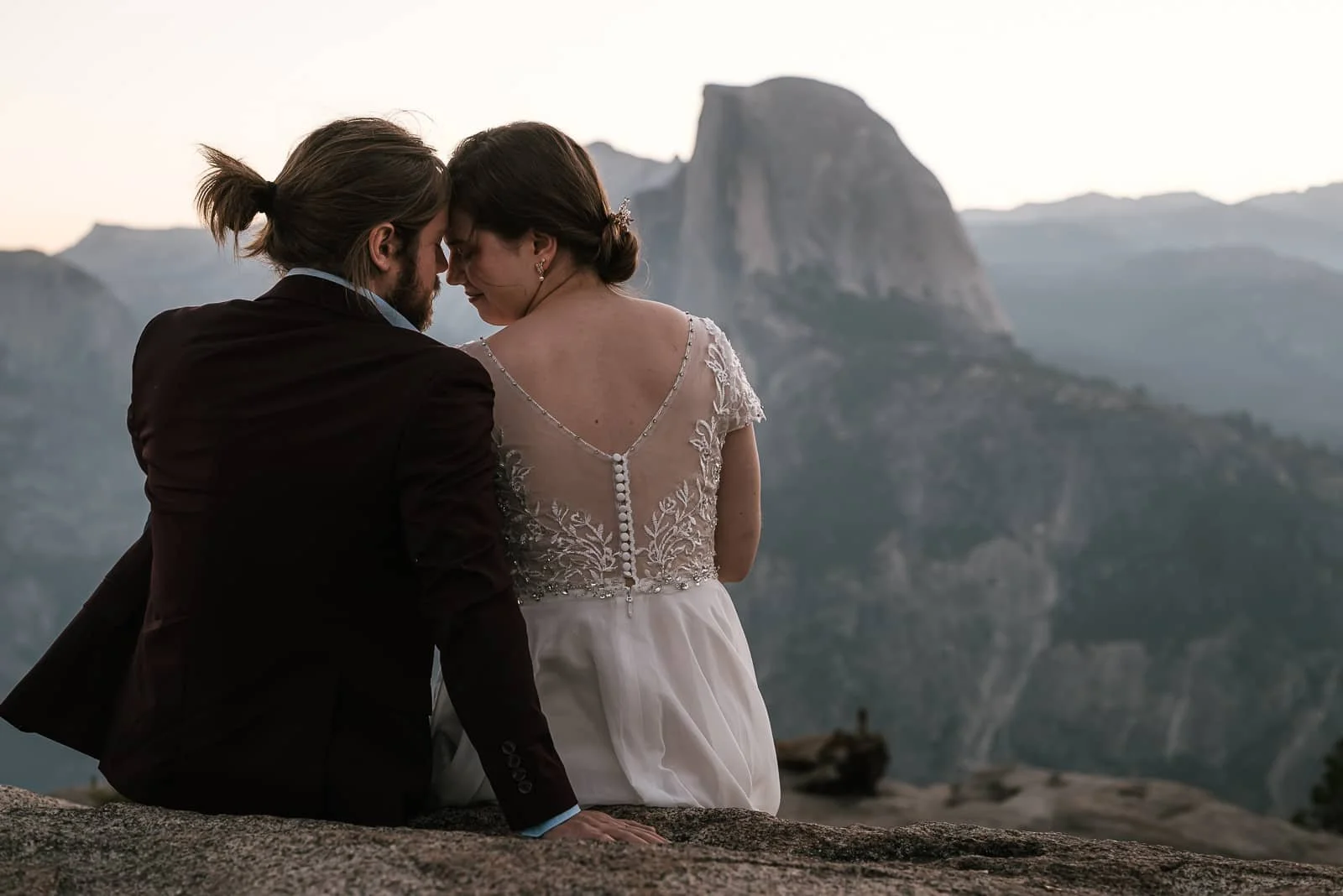 Couple leans in forehead to forehead with Half Dome in the background.