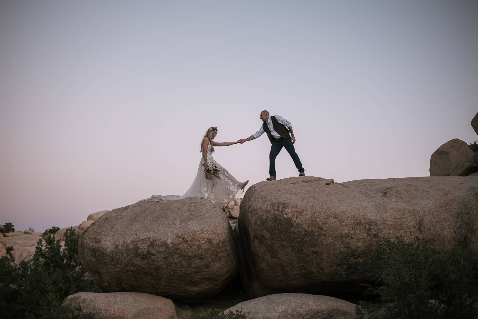 groom helps wife across boulder in joshua tree after elopement