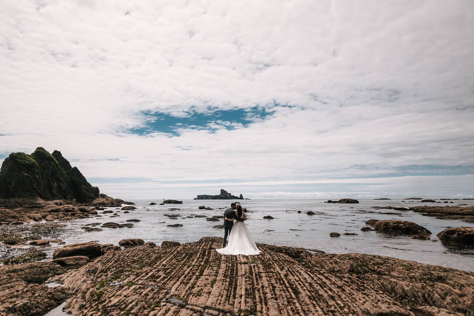 newlyweds hold each other for a kiss on the rocky shore of rialto beach