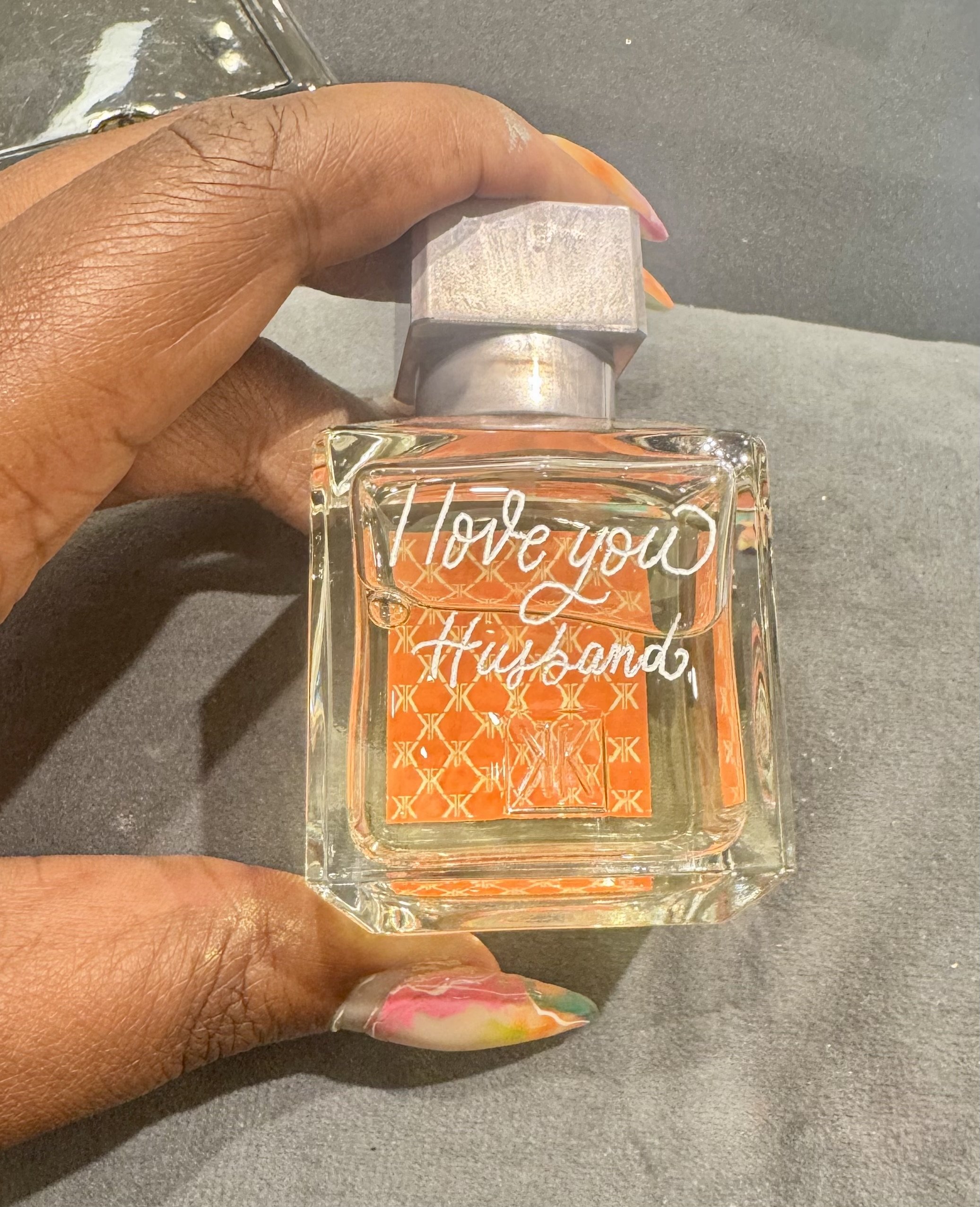 Hand holding a perfume bottle with the words 'Love you, Huband' written on it.