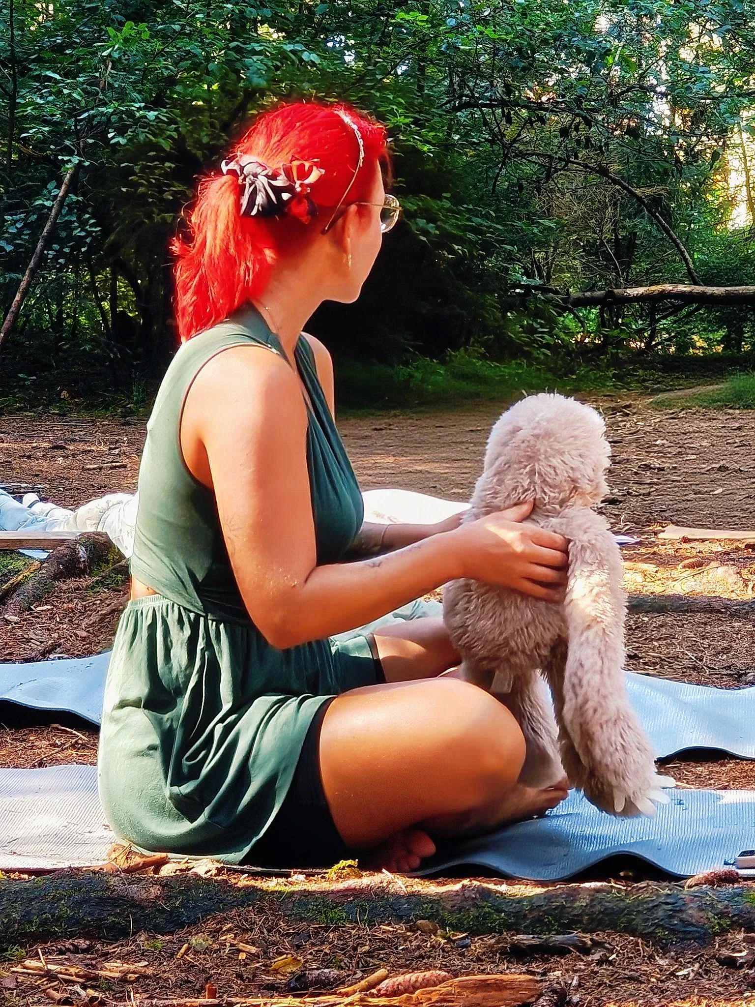 Die Kinderyogalehrerin Alja sitzt im Park auf einer Yogamatte, man sieht ihr leuchtend rotes Haar in der Sonne