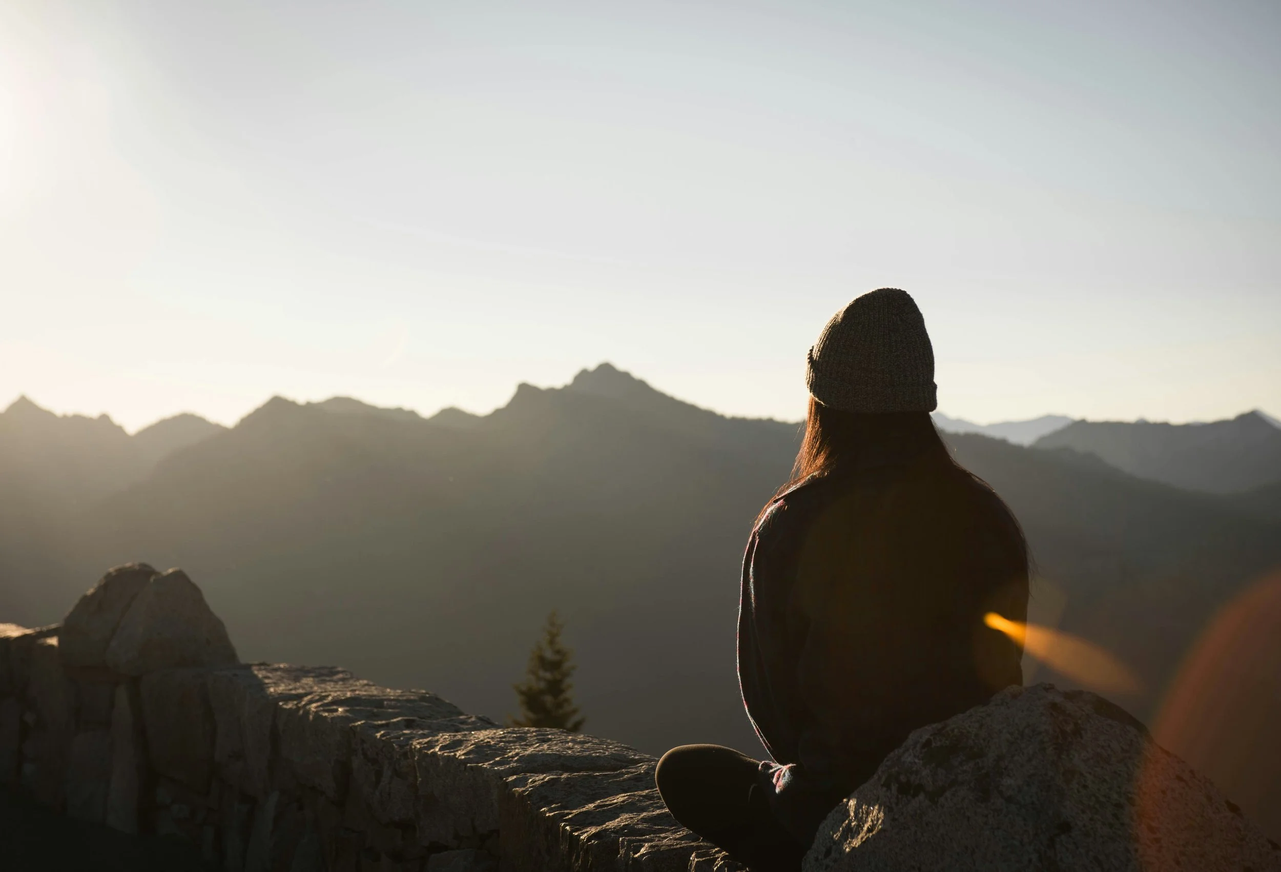 Eine Frau sitzt im Meditationssitz und blickt über die Berge