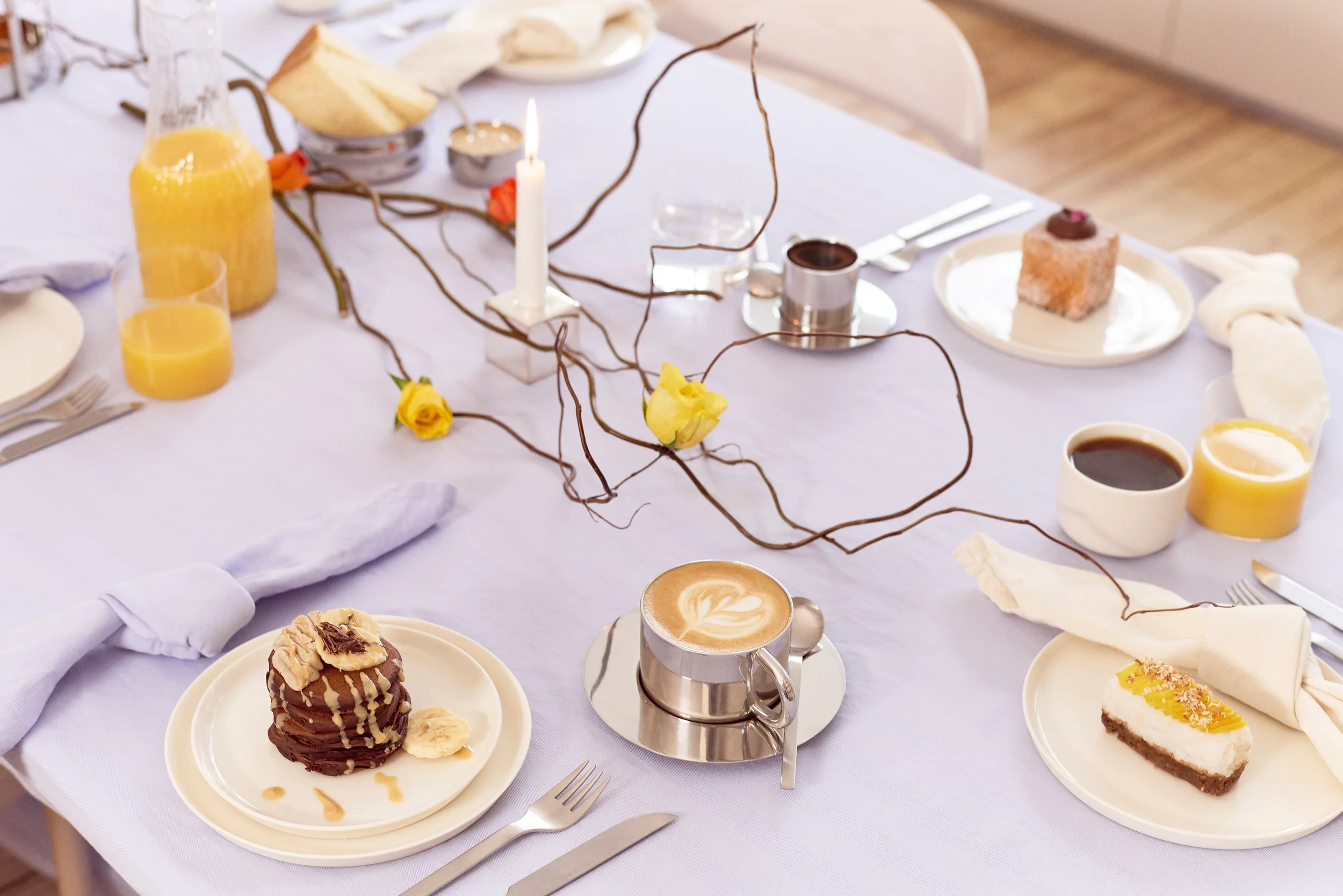 Ein schön gedeckter Tisch mit Fairtrade-Produkten wie Kaffee, Pancakes mit Bananen und Rosen ist hier zu sehen