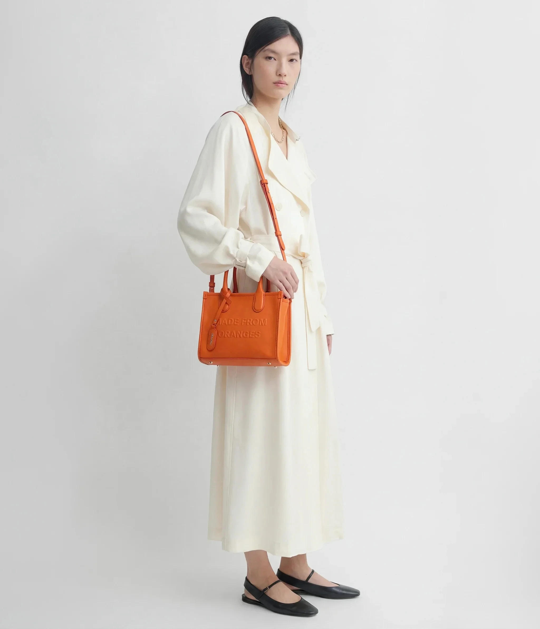 Ein Model trägt einen weißen Mantel und eine faire Tote Bag aus Orangenleder der Marke Miomojo