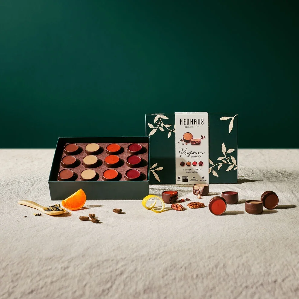 Die vegane Kollection Pralinen von Neuhaus choloates ist heir zu sehen, davor liegen Früchte und Kräuter