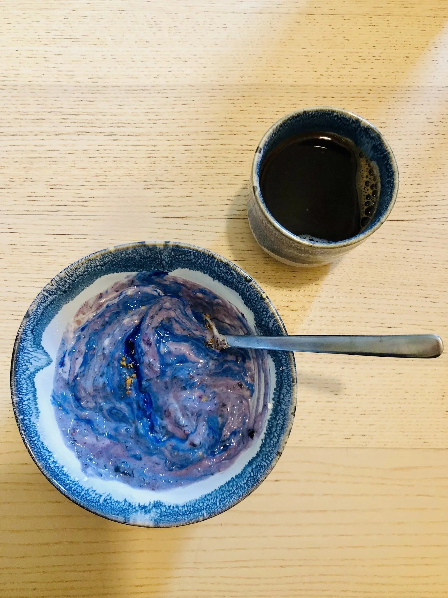 Eine Schüssel mit einem Frühstücks-Smoothie mit blauer Spirulina. Der Smoothie sieht aus wie das Weltall. Daneben steht ein becher Kaffee.