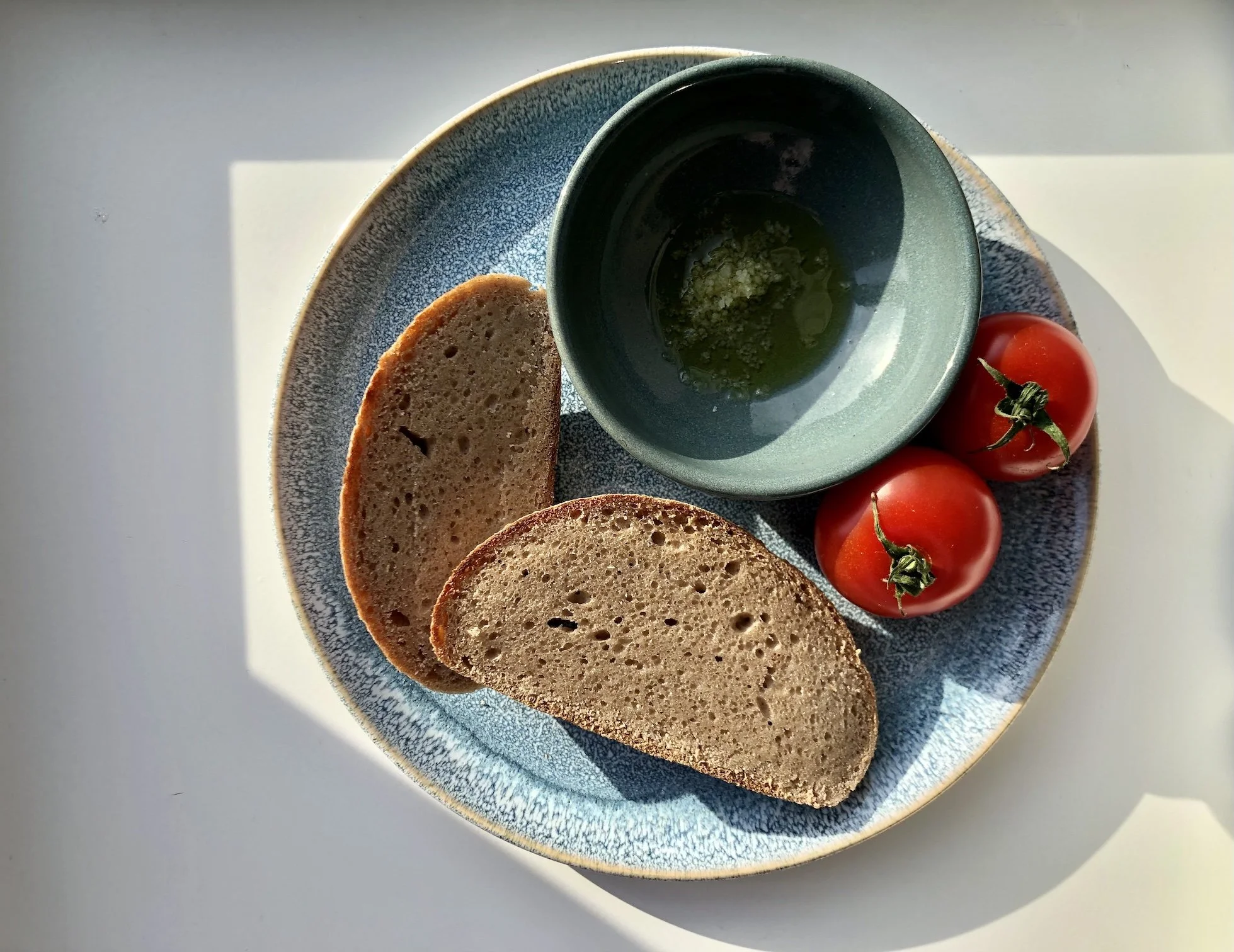 Das glutenfreie Krustenbrot von echt jetzt mit Salz, Öl und Tomaten auf einem Teller