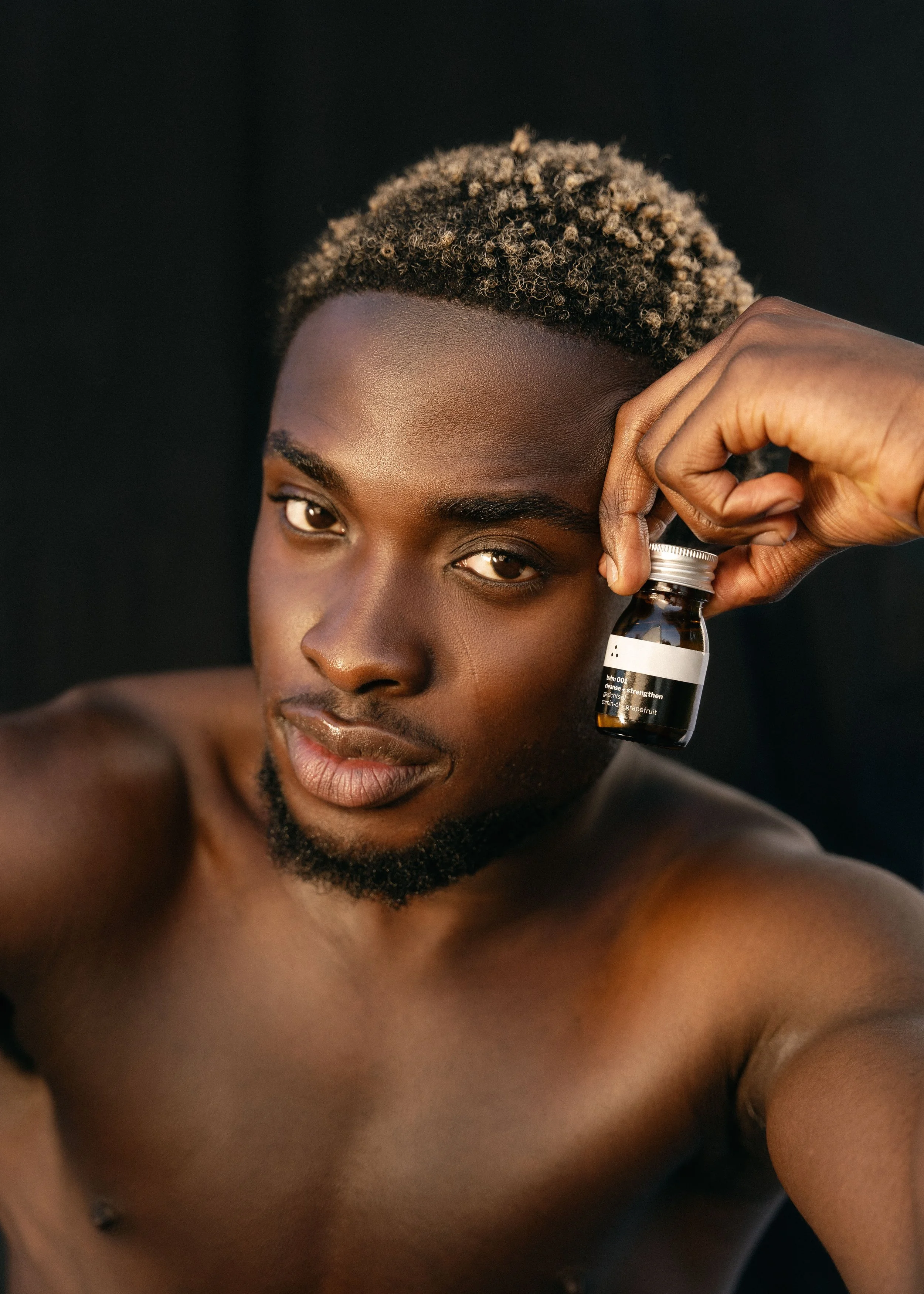 Ein männliches Model blickt in die Kamera und hält den toner 001 von therefore beauty in der Hand