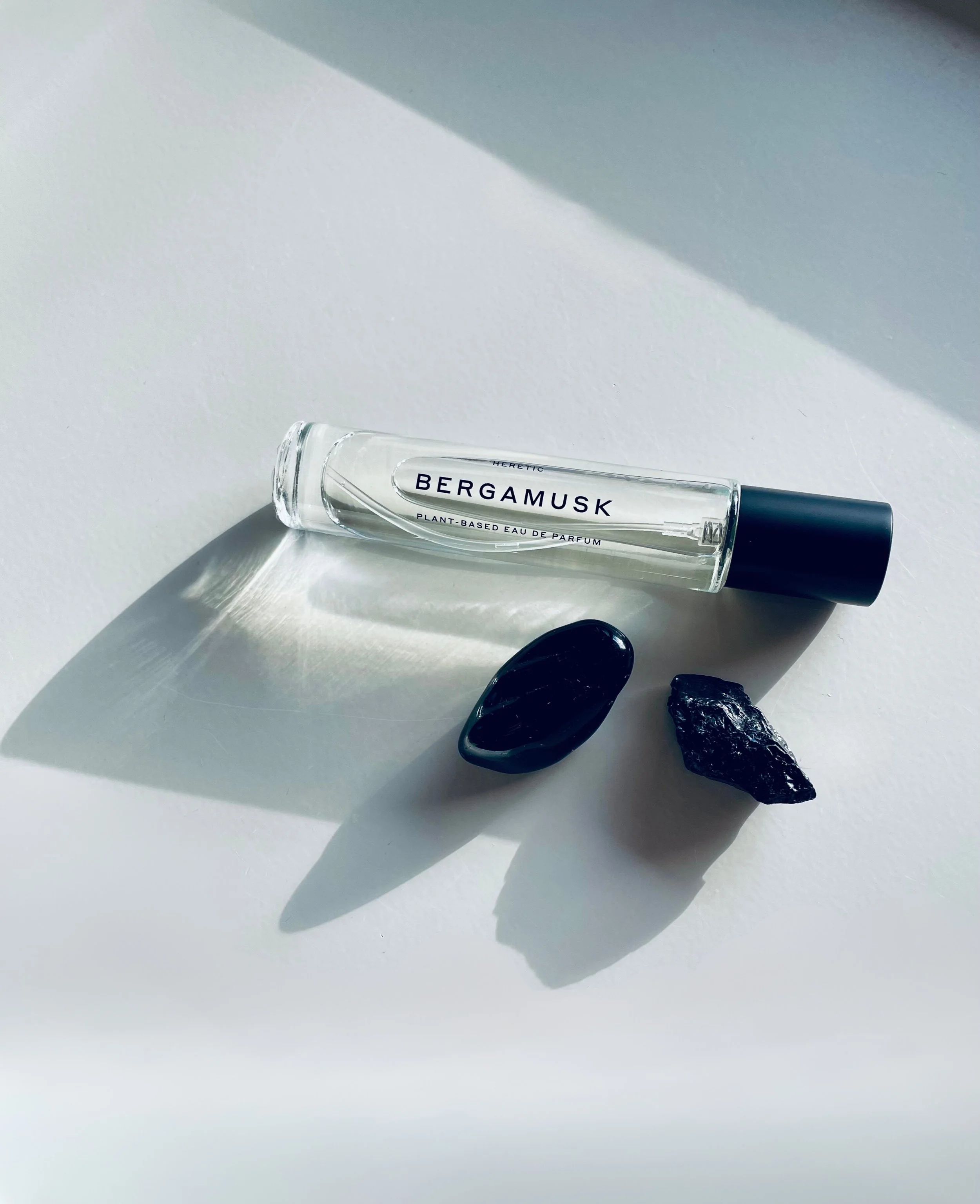 EIn Flakon Bergamusk der Naturkosmetik Marke Heretic liegt neben zwei schwarzen Kristallen