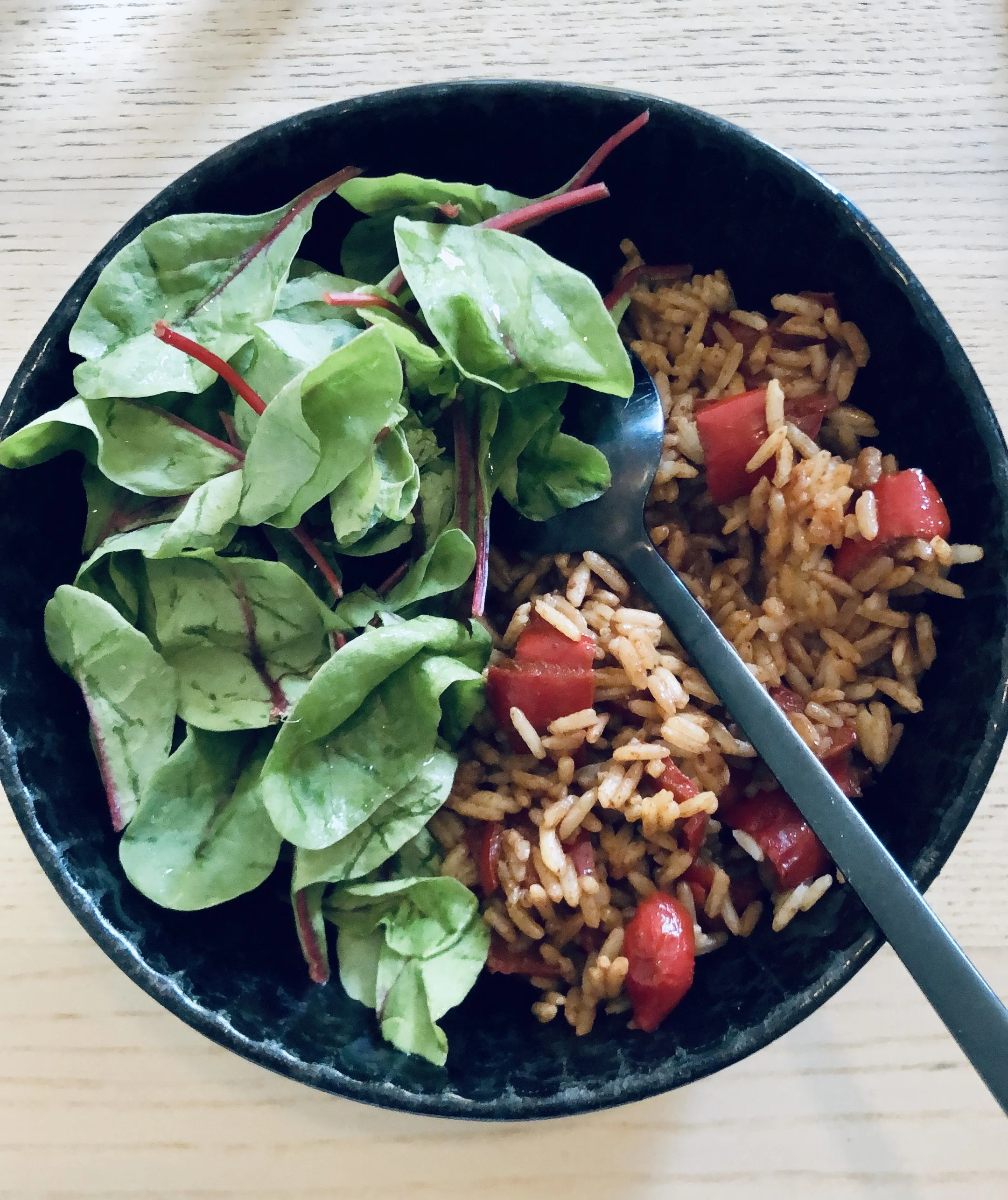 Eine schwarze Schüssel auf einem Tisch. Darin Spinat, Vollkornreis und Gemüse