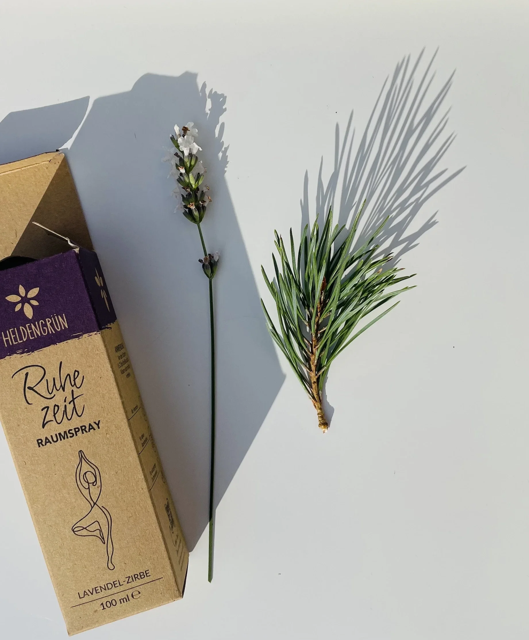 Die Verpackung vom Raumspray Ruhezeit von Heldengrün ist hier zu sehen, daneben liegen Lavendel und Zirbenzweige