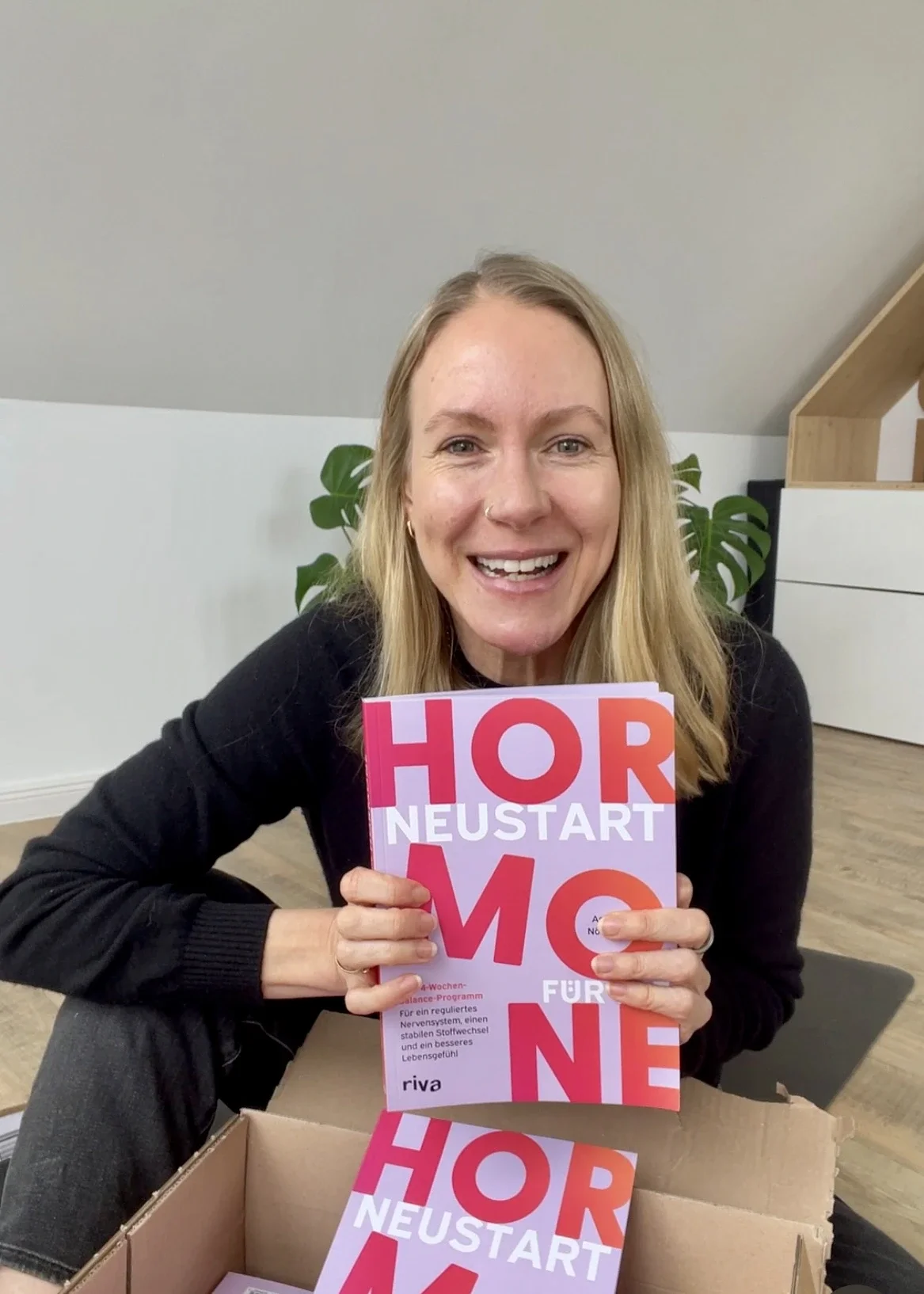 Autorin Astrid Nöhring hält ihr Buch "Neustart für die Hormone" in den Händen und lacht in die Kamera