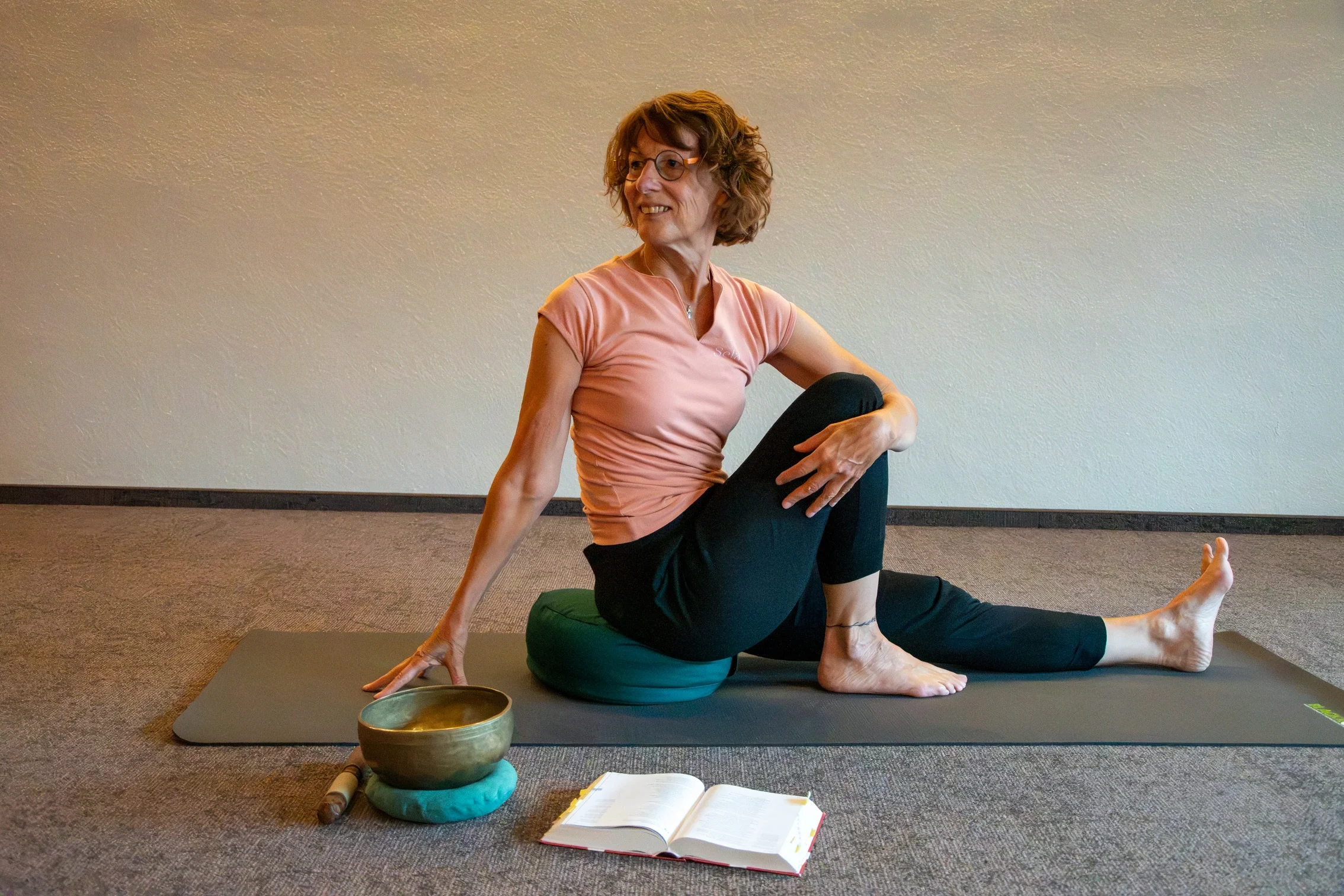Die Yogalehrerin Maria Schotte sitzt im Drehsitz auf einer Matte. Vor ihr liegt eine Bibel.