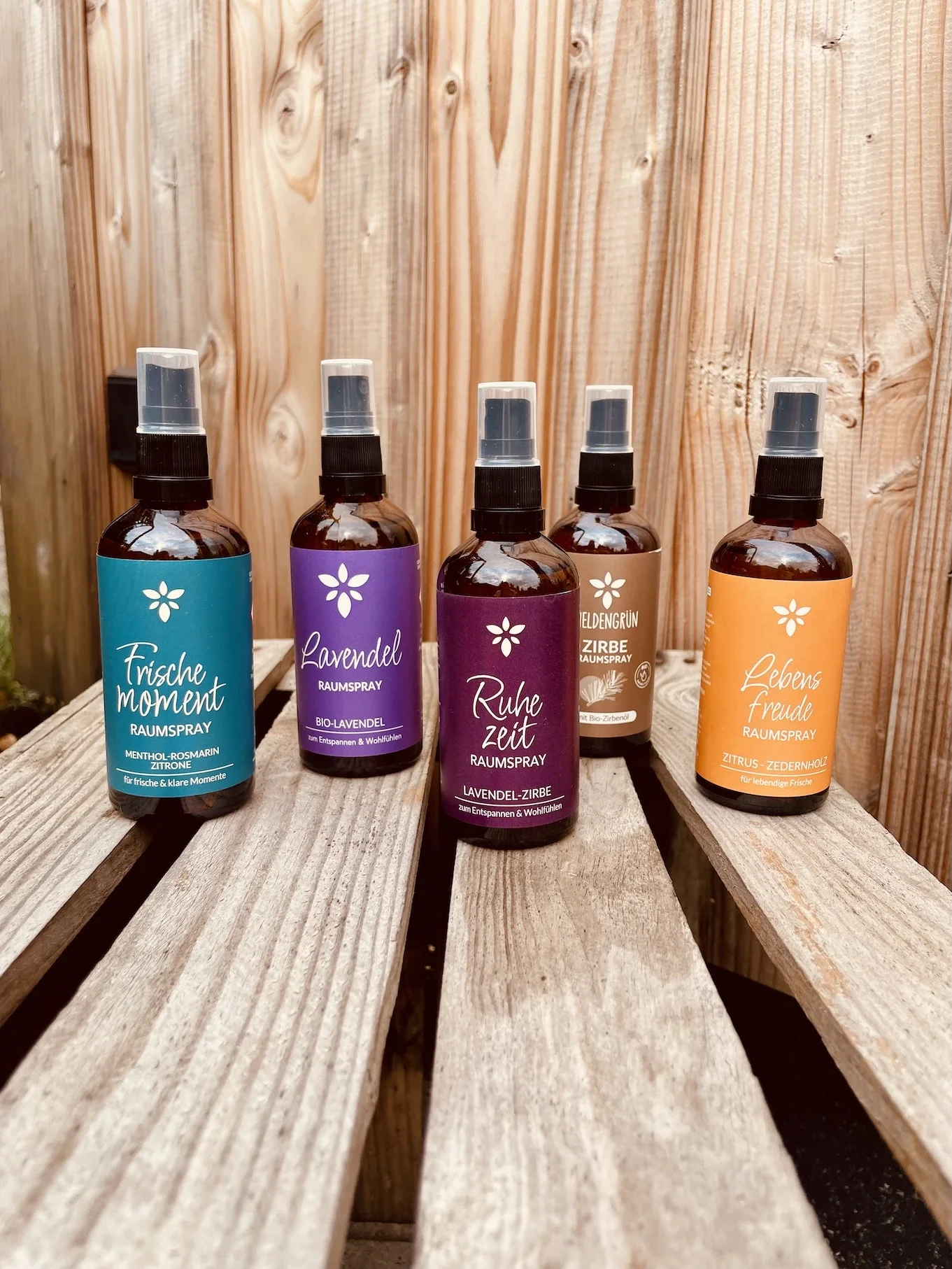Die ätherischen Öle-Raumsprays der Marke Heldengrün stehen hier aufgereiht auf einer Holzkiste an einer Holzwand