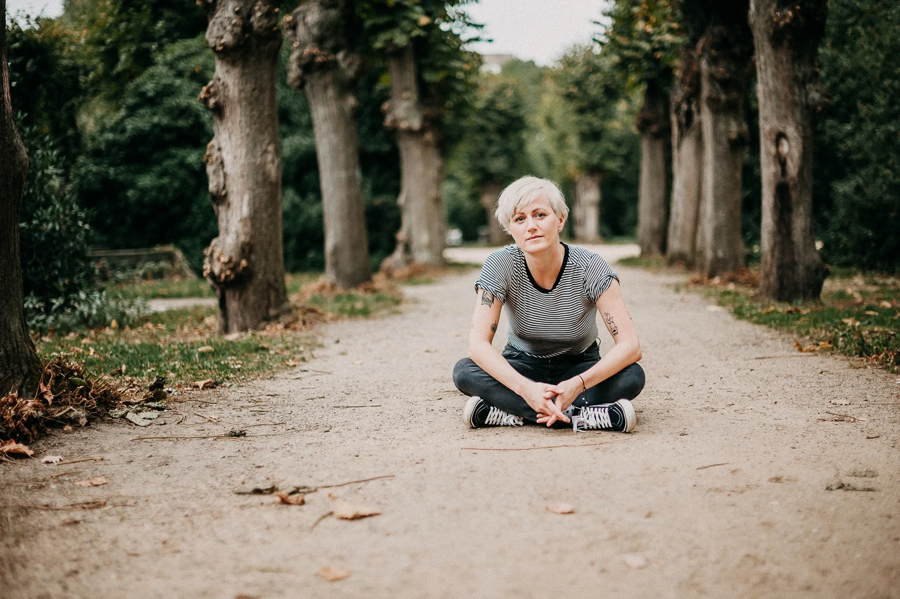 Die Psychoonkologische Gesprächstherapeutin und Yogalehrerin Tina Scheid sitzt auf einem Boden im Park und blickt in die Kamera