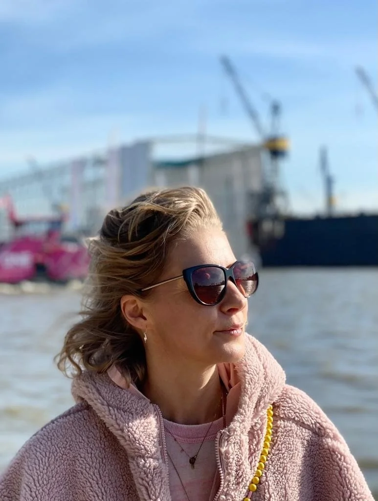 Anna Rech steht an der sonnigen Elbe, im Hintergrund sieht man Kräne