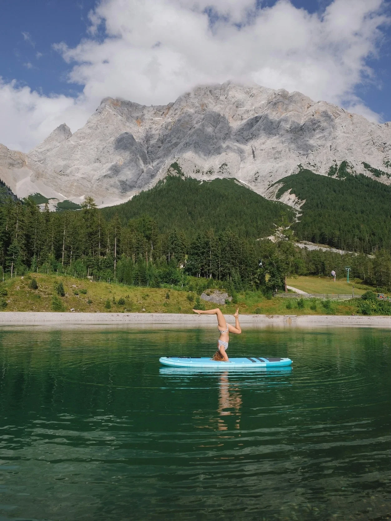 Eine Person übt einen Yoga-Kopfstand auf einem SUP, vor traumhafter Kulisse an einem Bergsee