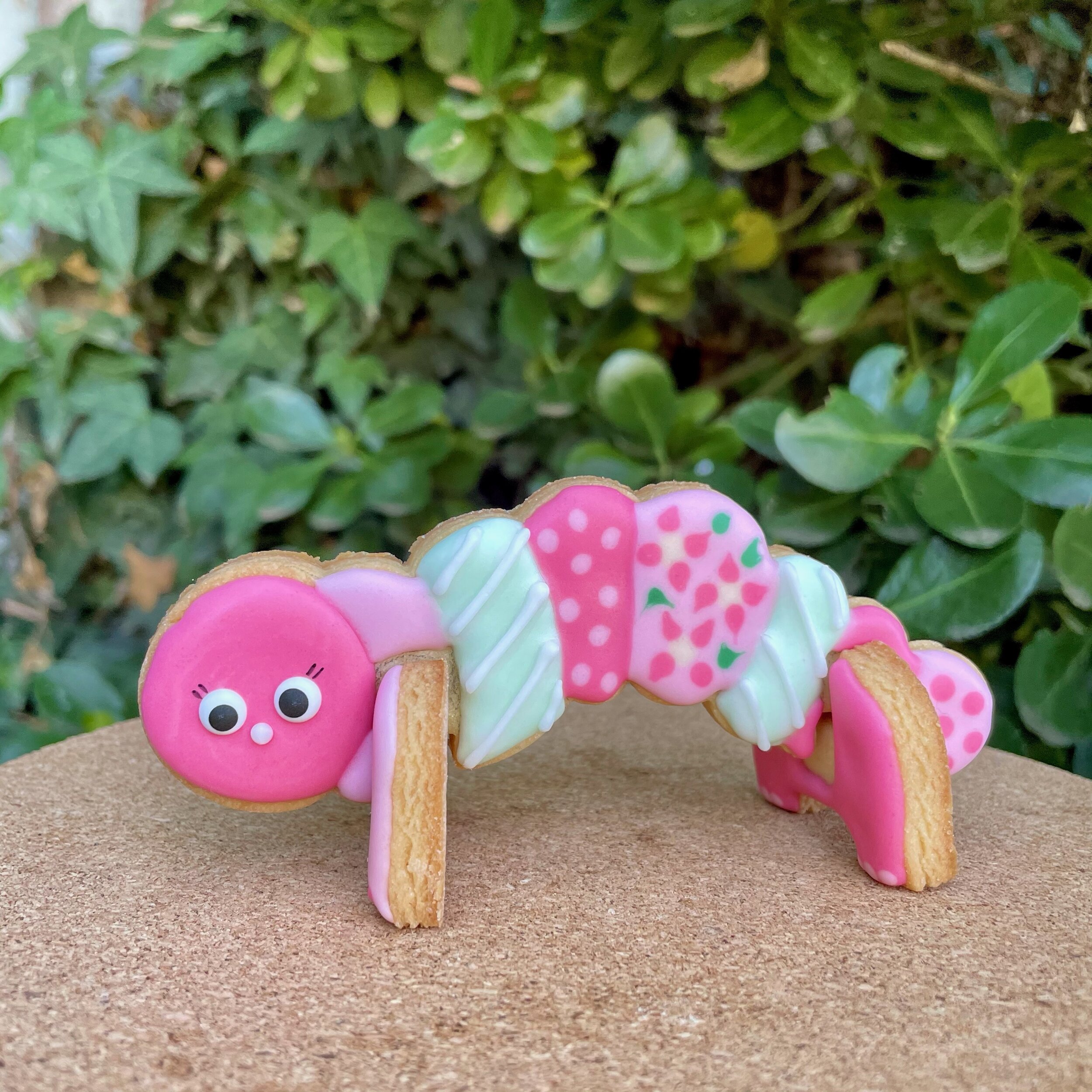 A 3D caterpillar cookie decorated with shades of varying pink icing