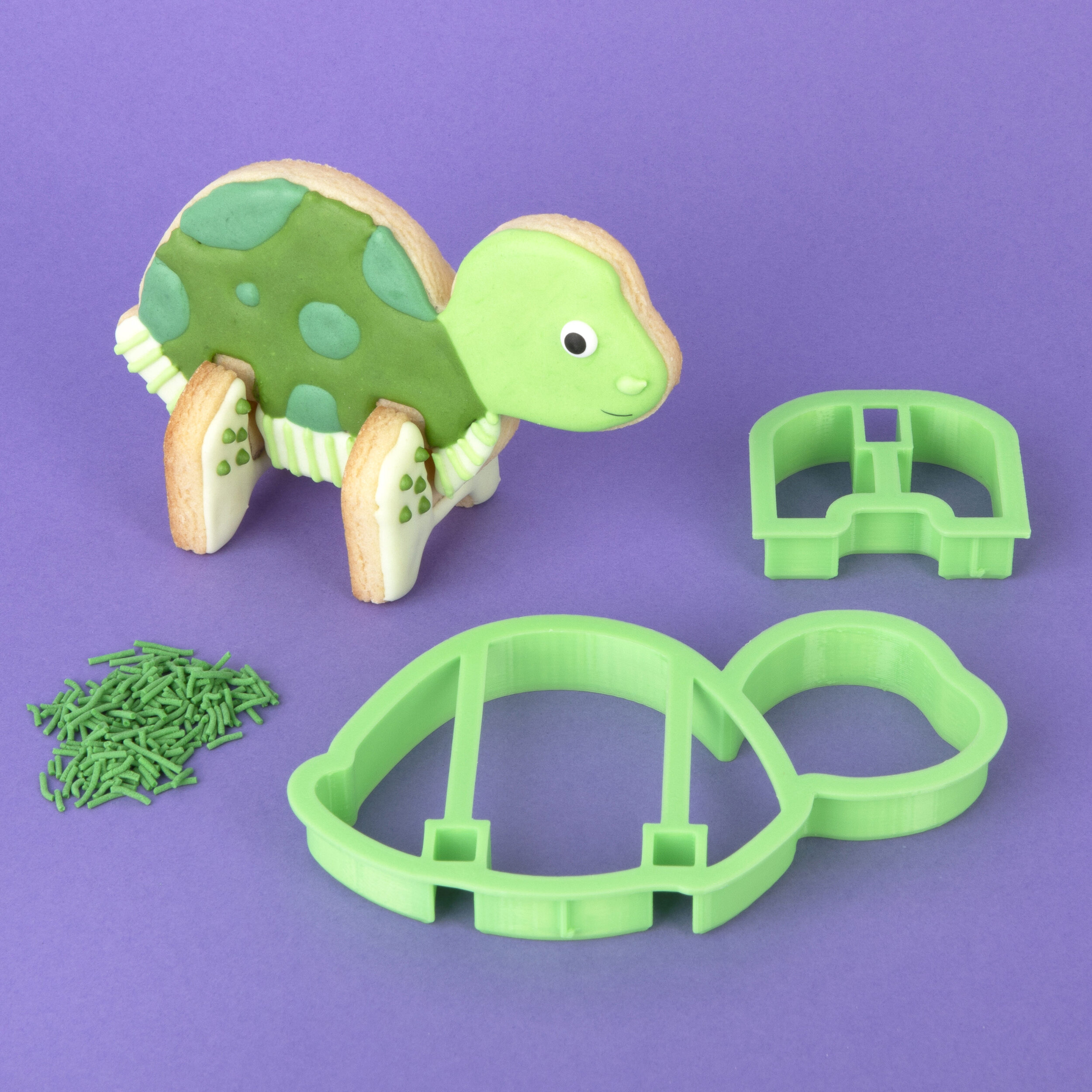 A decorated 3D turtle cookie standing next to the turtle cookie cutter