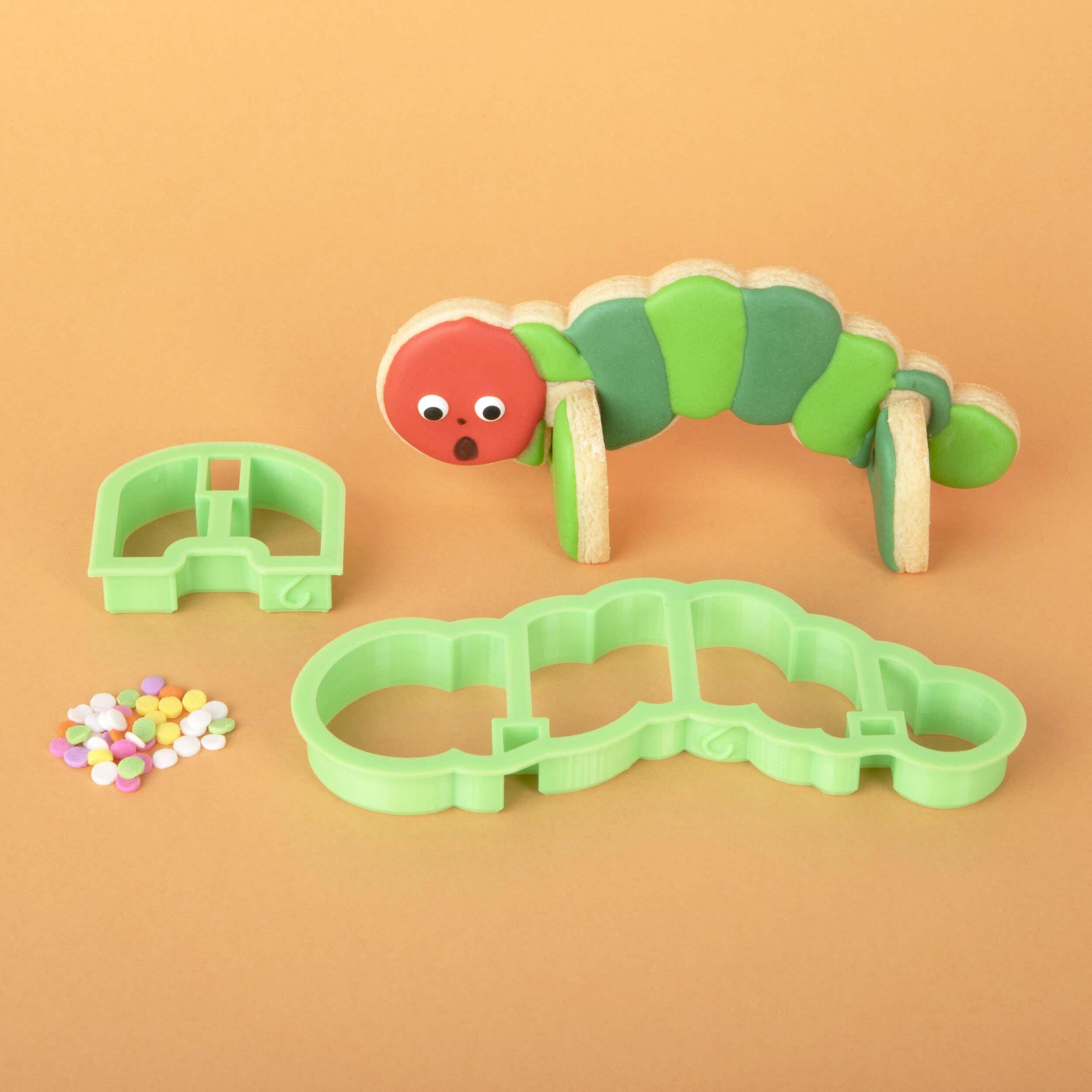 A decorated 3D caterpillar cookie standing next to the caterpillar cookie cutter