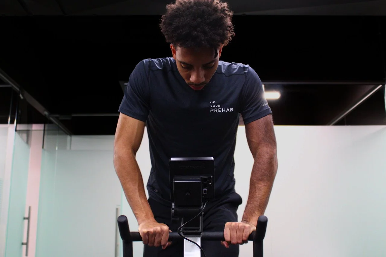 A young man working out on an exercise bike in a gym.