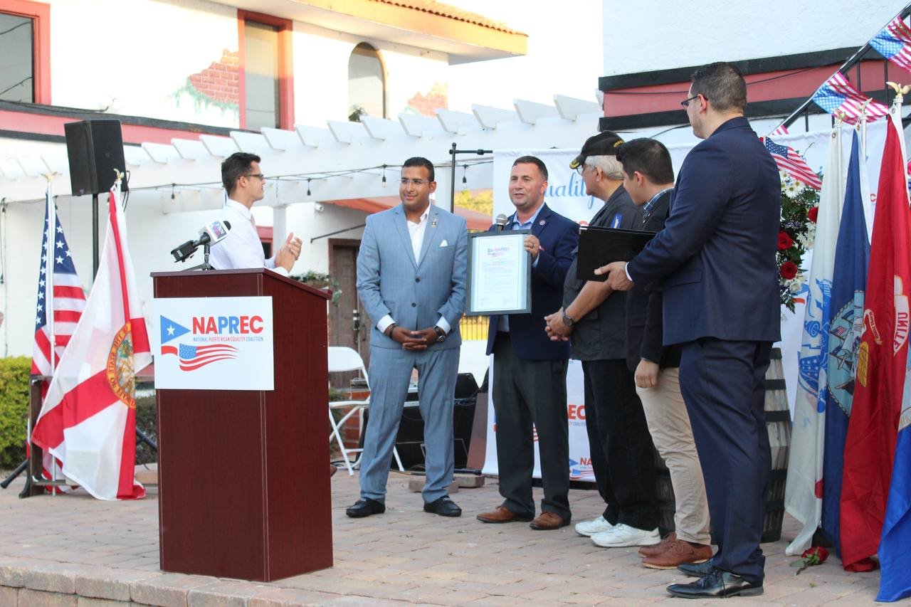 Participants at a NAPREC community event beside a podium and flags.
