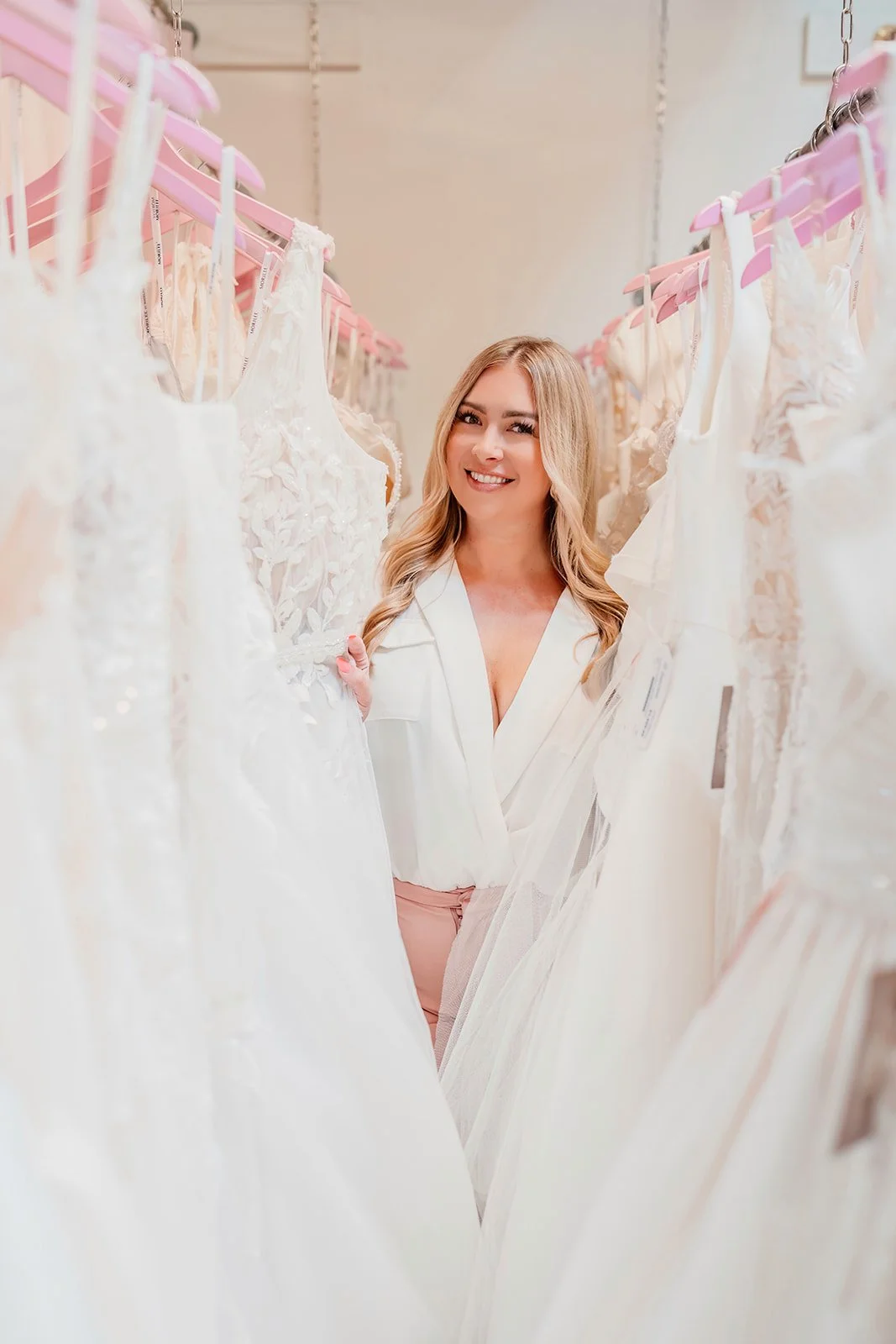 Ashley A., owner and bridal stylist at The Wedding Bell in Tacoma, standing in front of wedding gowns.