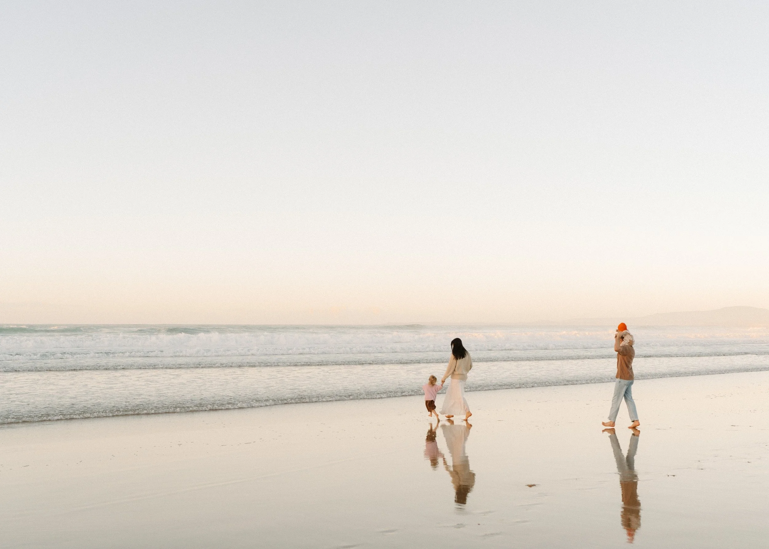Family walking along the beach at sunset with the ocean waves and sky in the background.