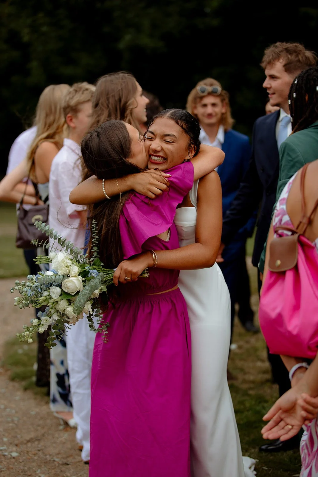 une mariée enlace une de ses amies qui porte une robe rose magenta