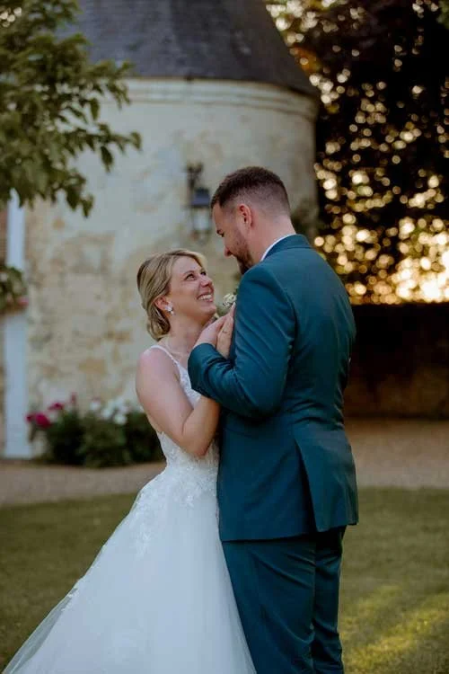 couple de mariés debout dans un parc d'un château au coucher du soleil se regardent en souriant