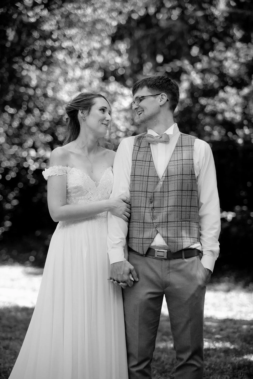 couple de mariés debout dans un parc se regardent en souriant en noir et blanc