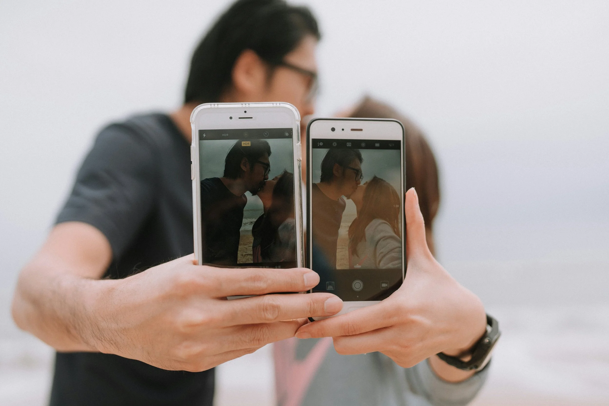 Image of a couple taking selfies on their cell phones of them kissing on a beach