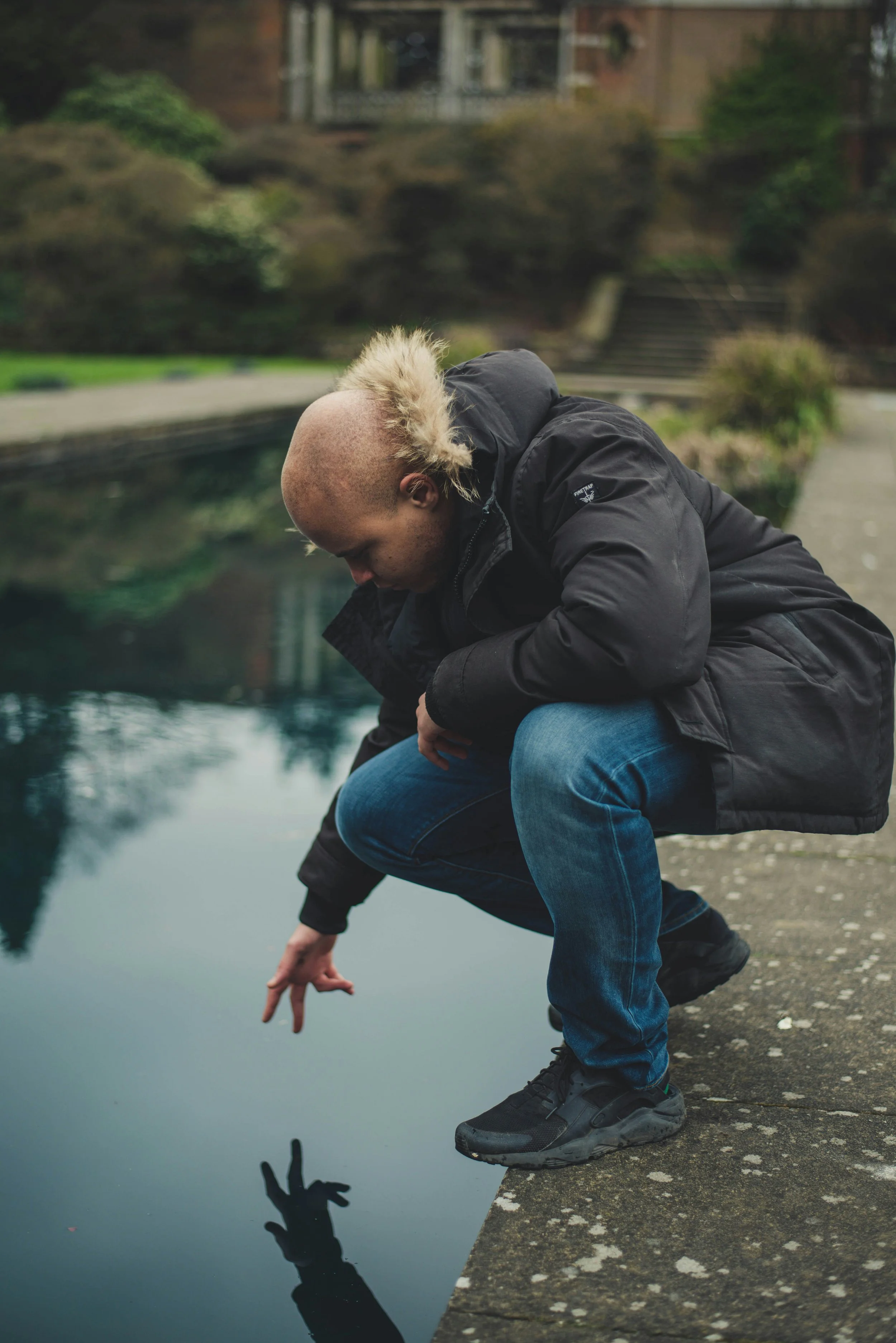 Man crouching beside a body of water an reaching toward their reflection, creating a moment of self-recognition and reflection.