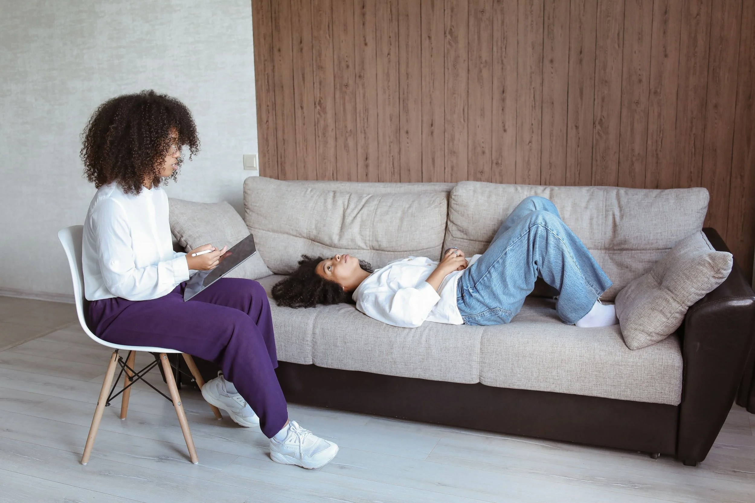 Therapist takes notes while a client lies on a couch during a psychotherapy session in a calm, modern office.