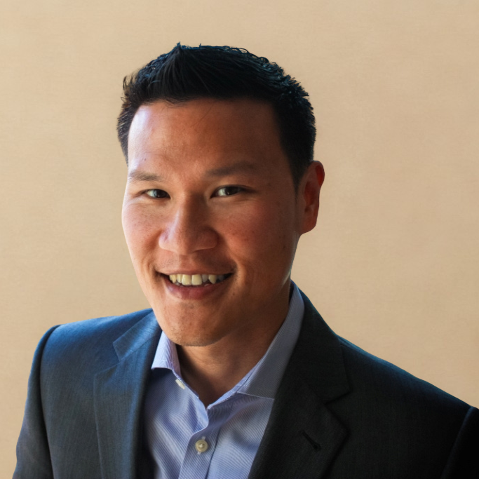 Ricky Weng stands up in front of a beige background smiling wearing a light blue casual shirt and a navy blue blazer.