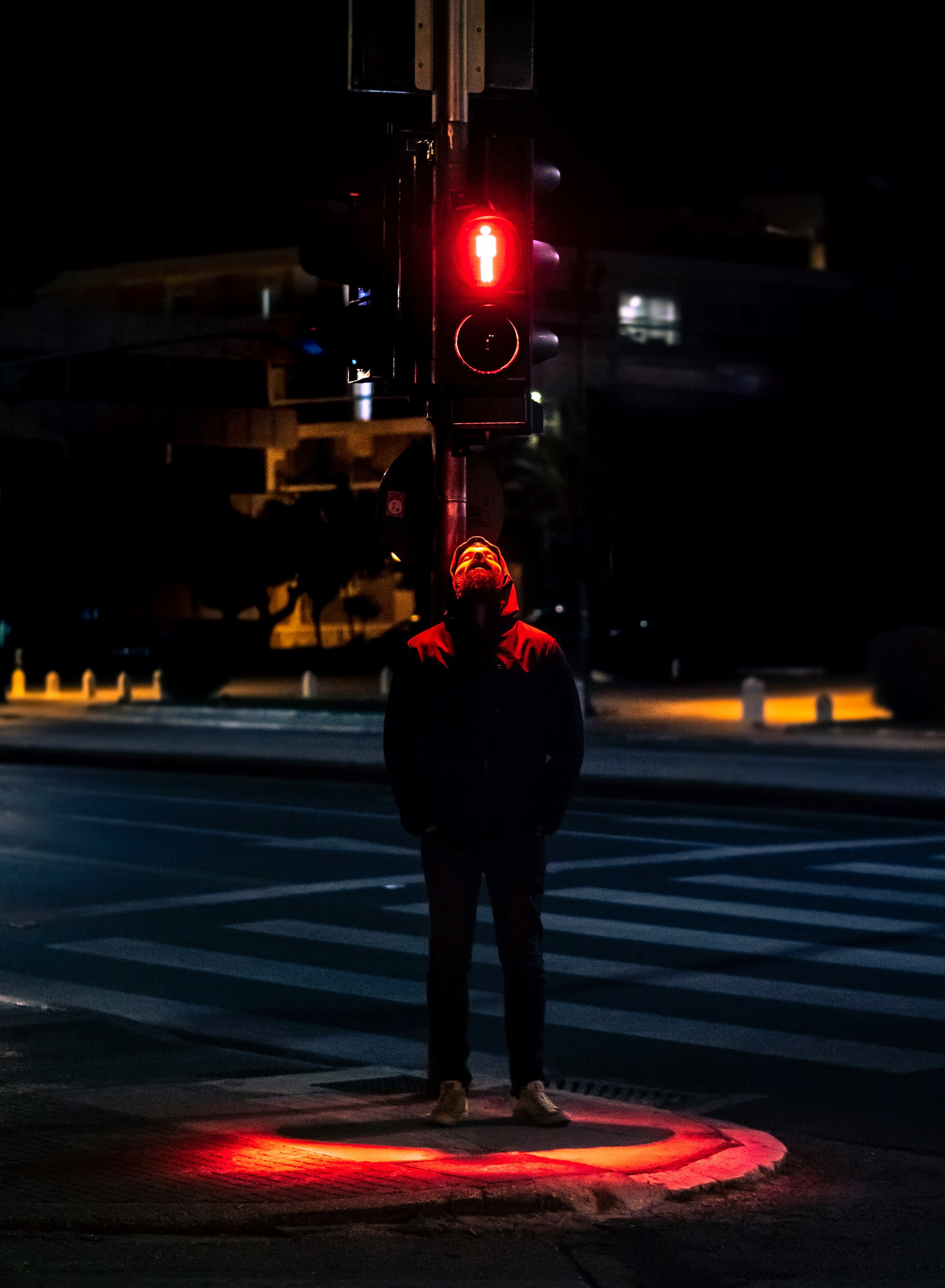 Person standing under a red pedestrian signal at night near a crosswalk.