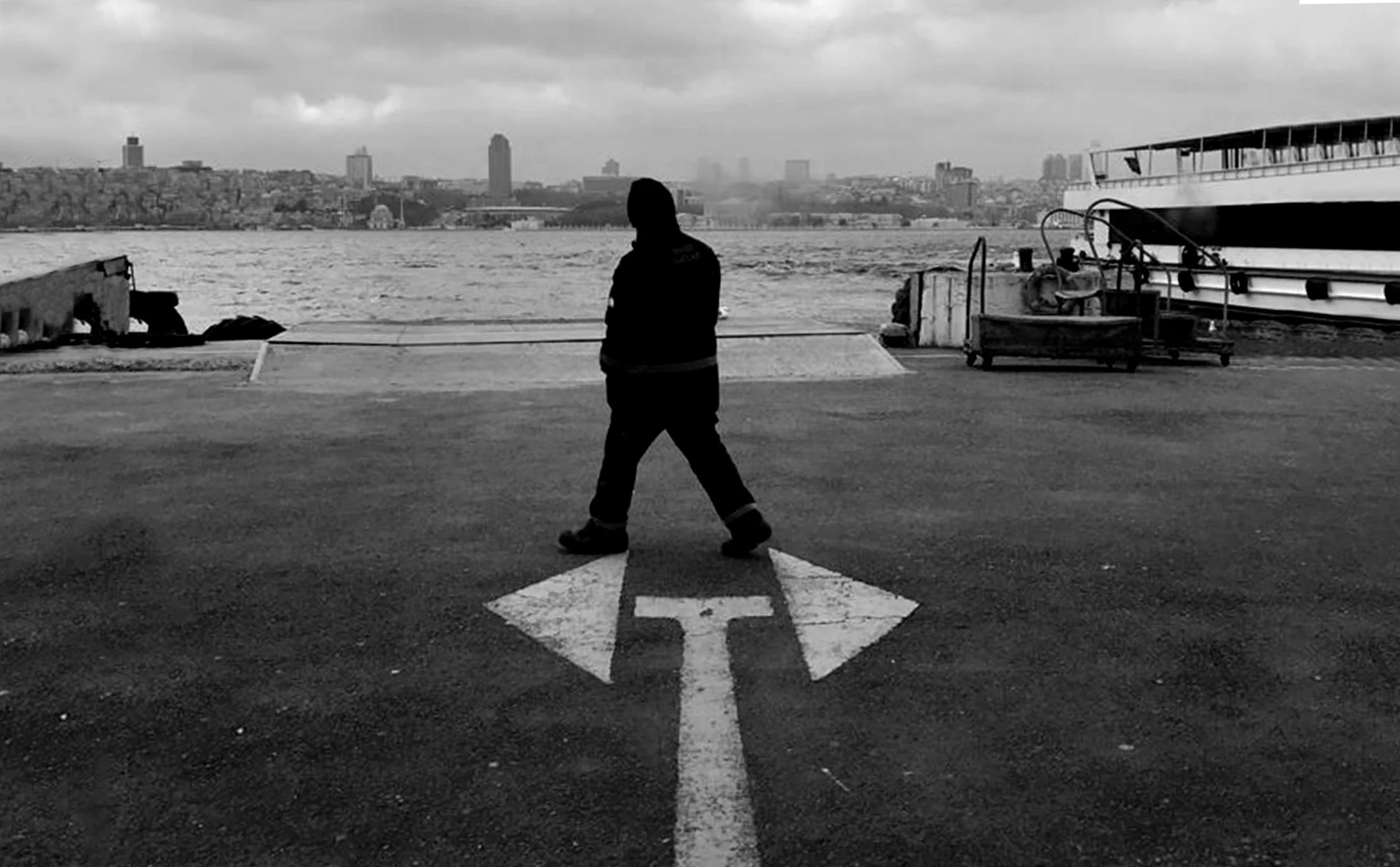 Person walking across a large arrow painted on the ground near the water.
