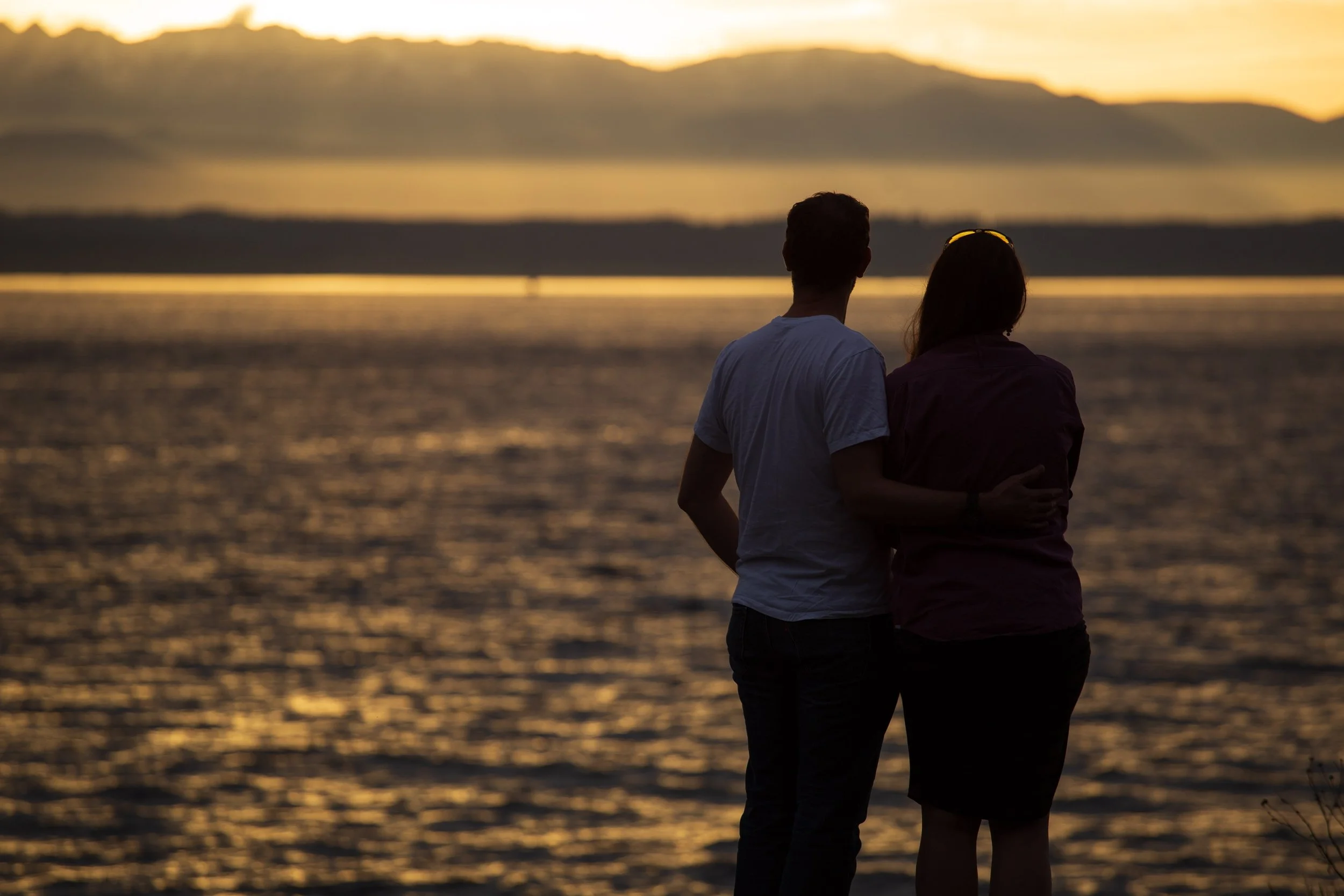 A white couple looking out over the ocean embracing their partnership.