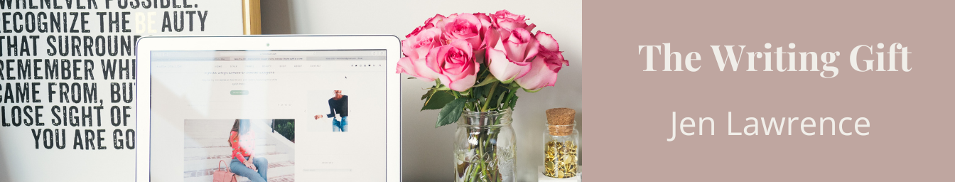 Open laptop, vase with pink roses, and small glass bottle with gold paper inside on a desk. Behind, framed text art and a gray wall. On right, book cover of 'The Writing Gift' by Jen Lawrence.