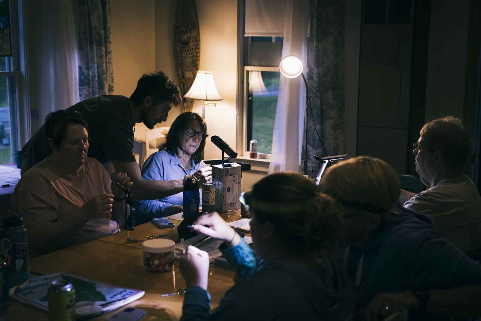  Dom (he/him) guides campers by lamp light through fly tying patterns, gathered around a large table at Evan’s Notch Lodge. Photo:  Joe Klementovich  